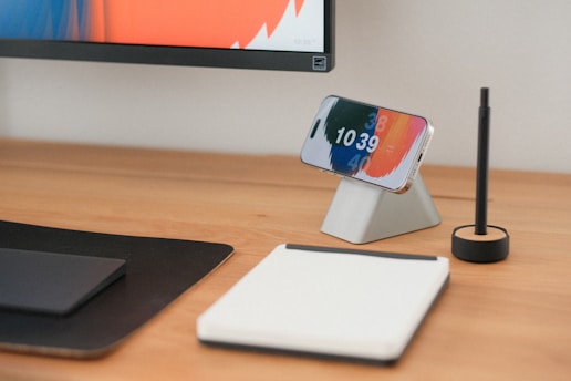 A phone, pad, and pen sit on a wooden desk.