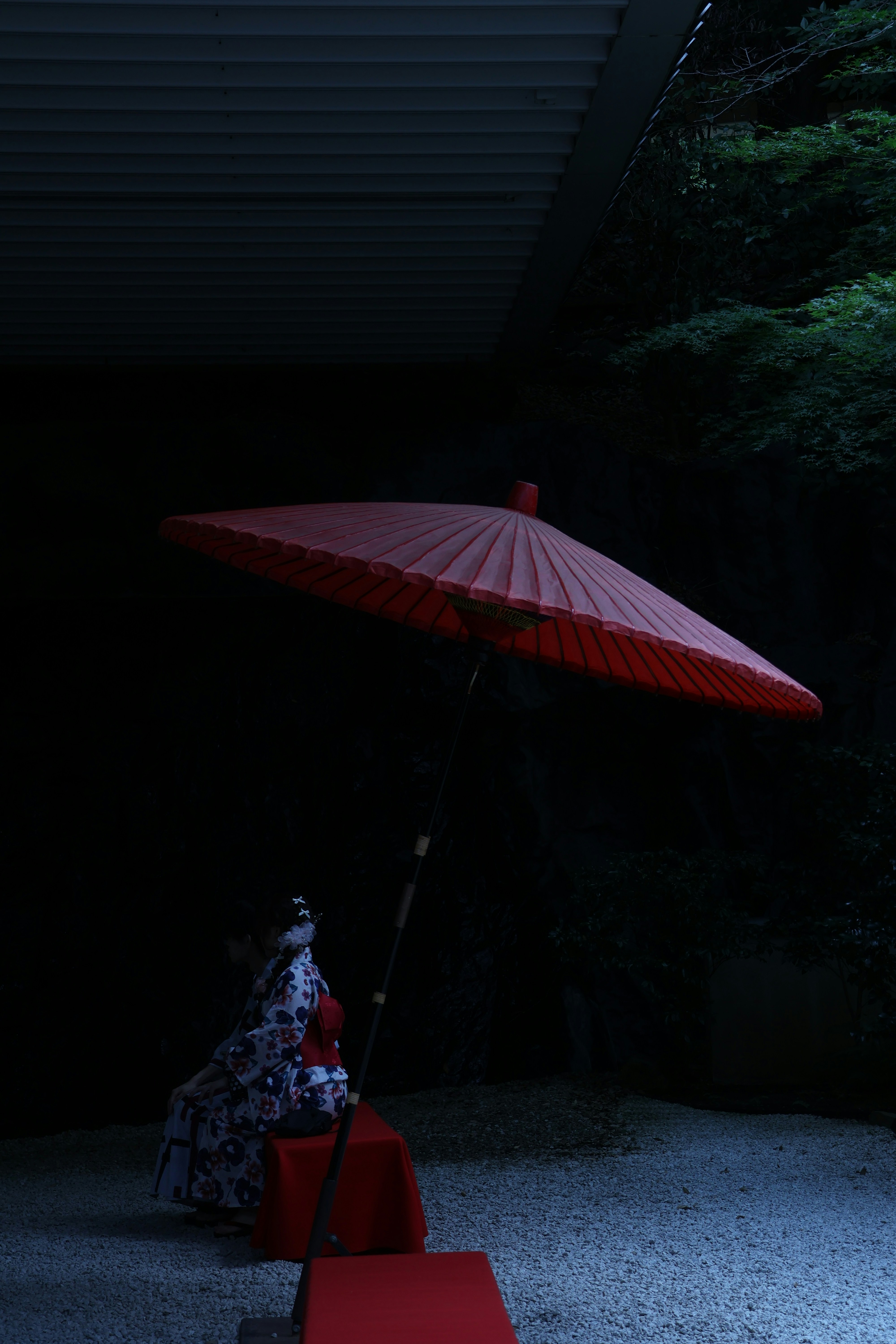 A woman sits beneath a red umbrella.