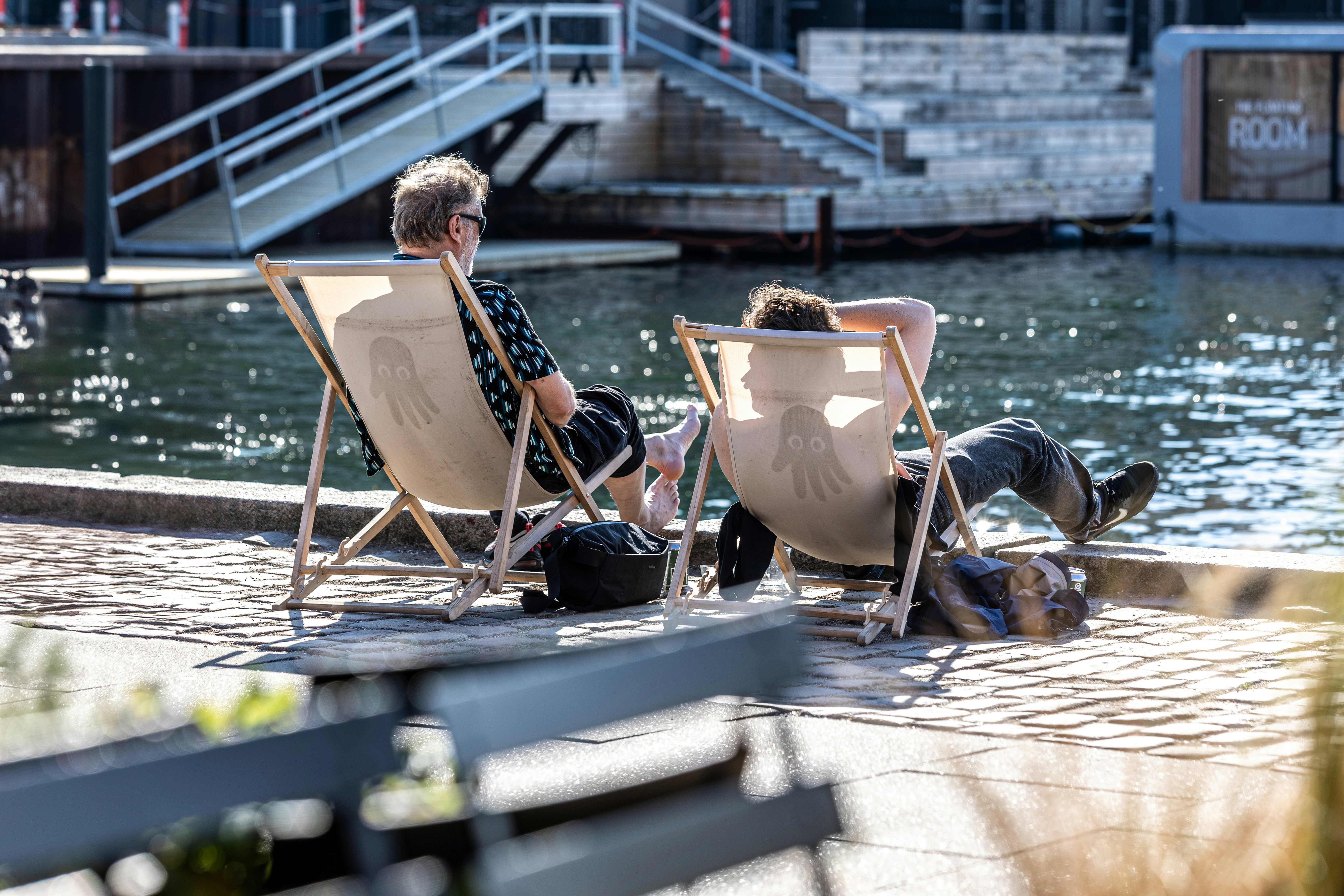 Zwei Personen entspannen sich auf Stühlen am Wasser.
