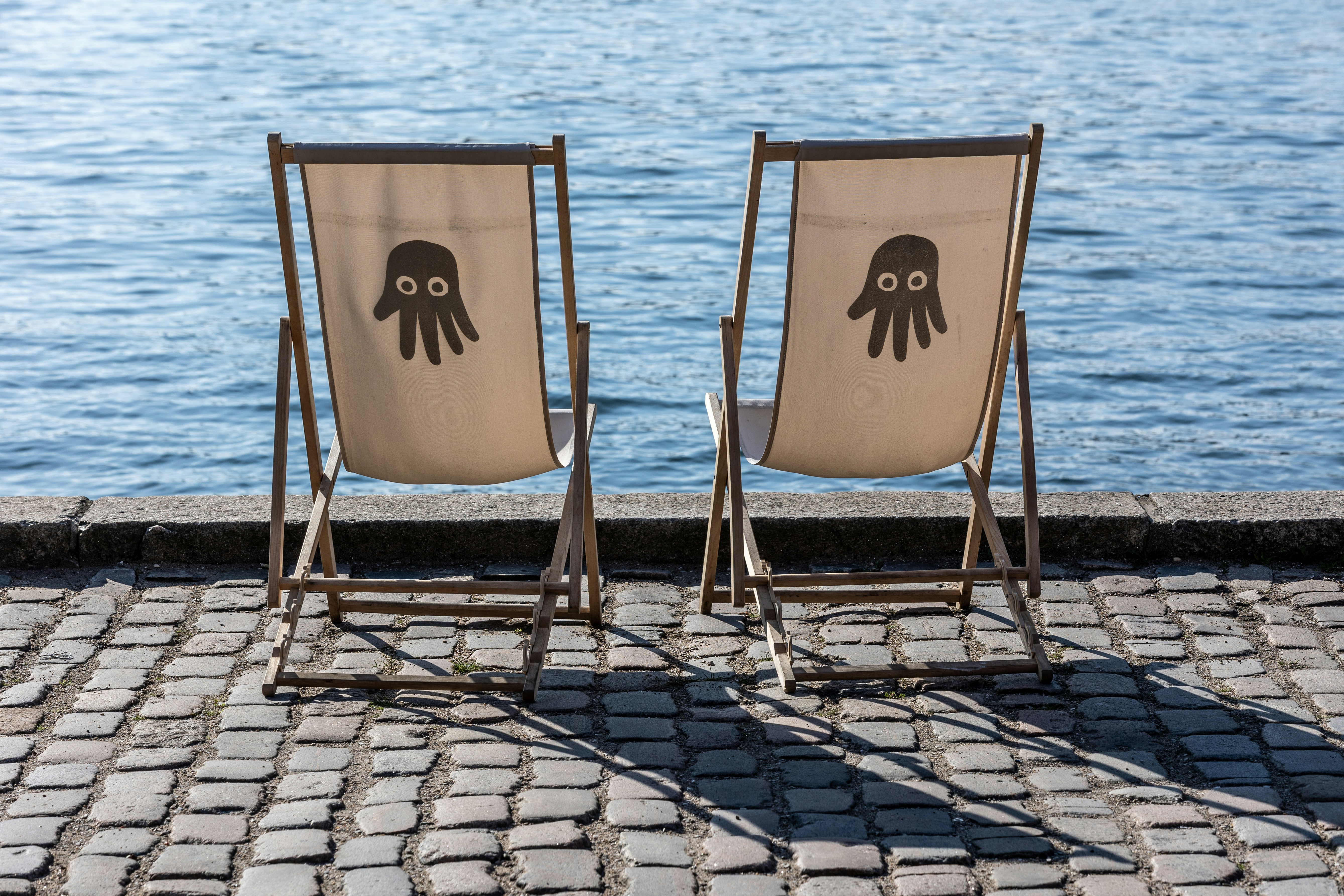 Zwei Liegestühle stehen am Wasser.