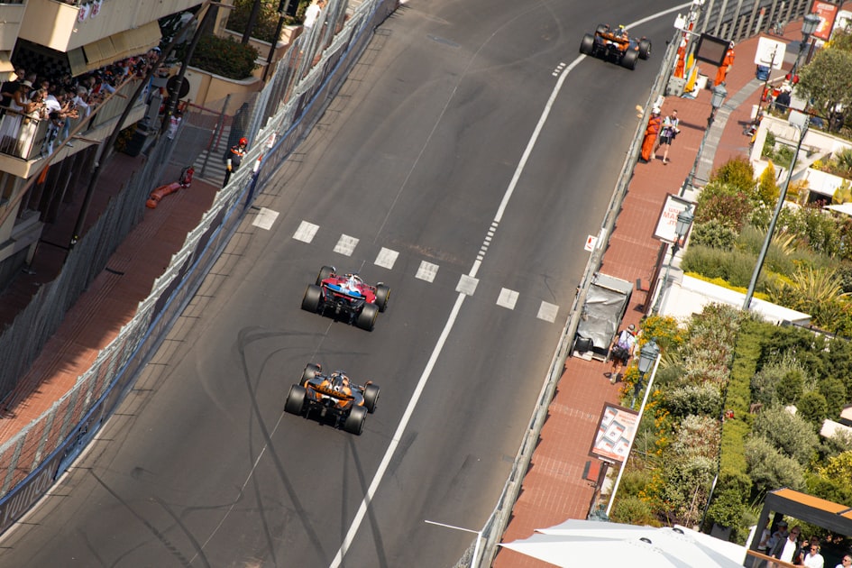 Formula 1 Ferrari and McLaren cars racing through Monaco's tight street circuit with fans watching from balconies