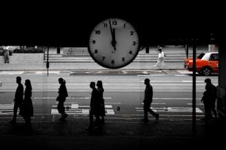 People walk by a clock on a busy street.
