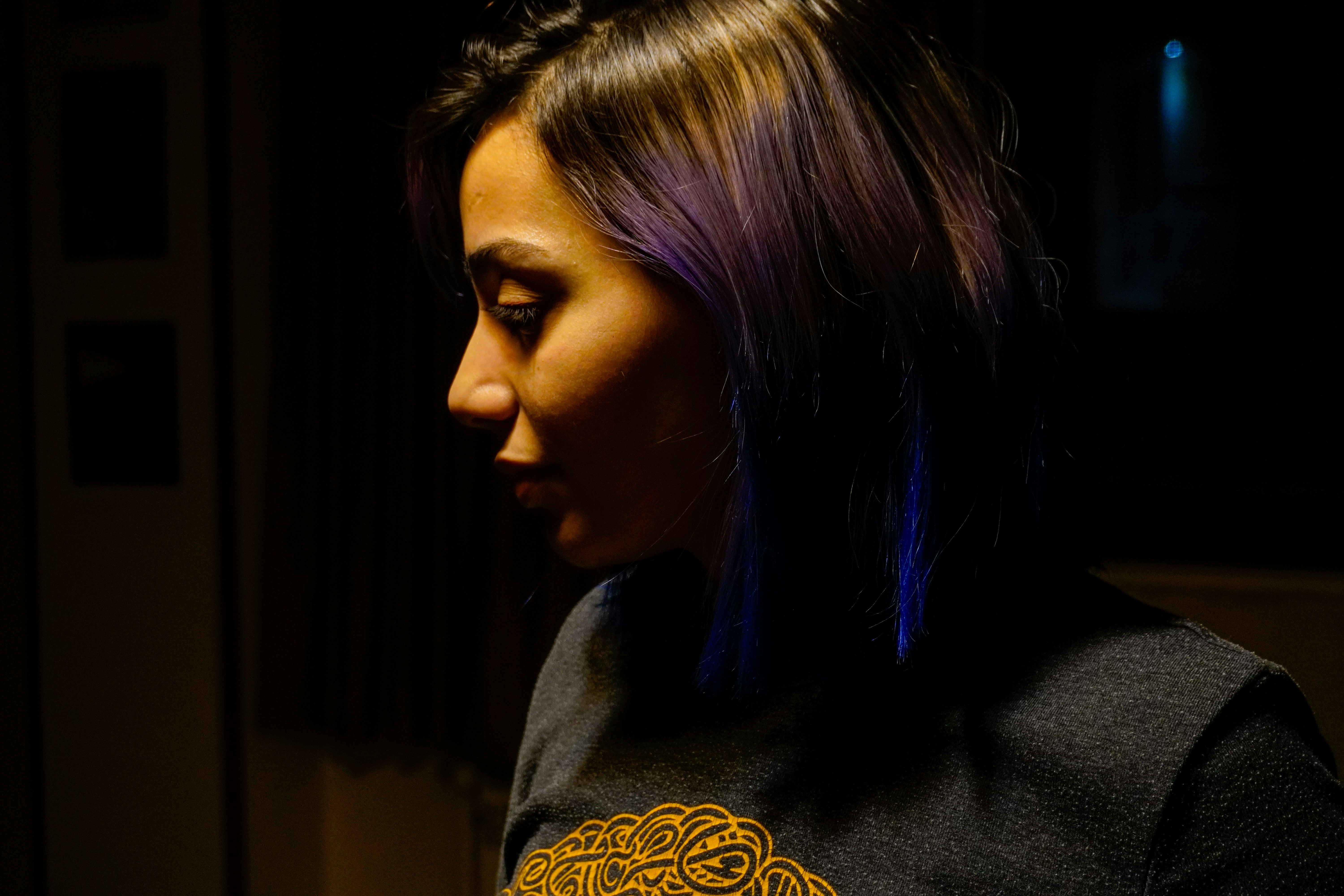 A woman with purple hair poses in low light.