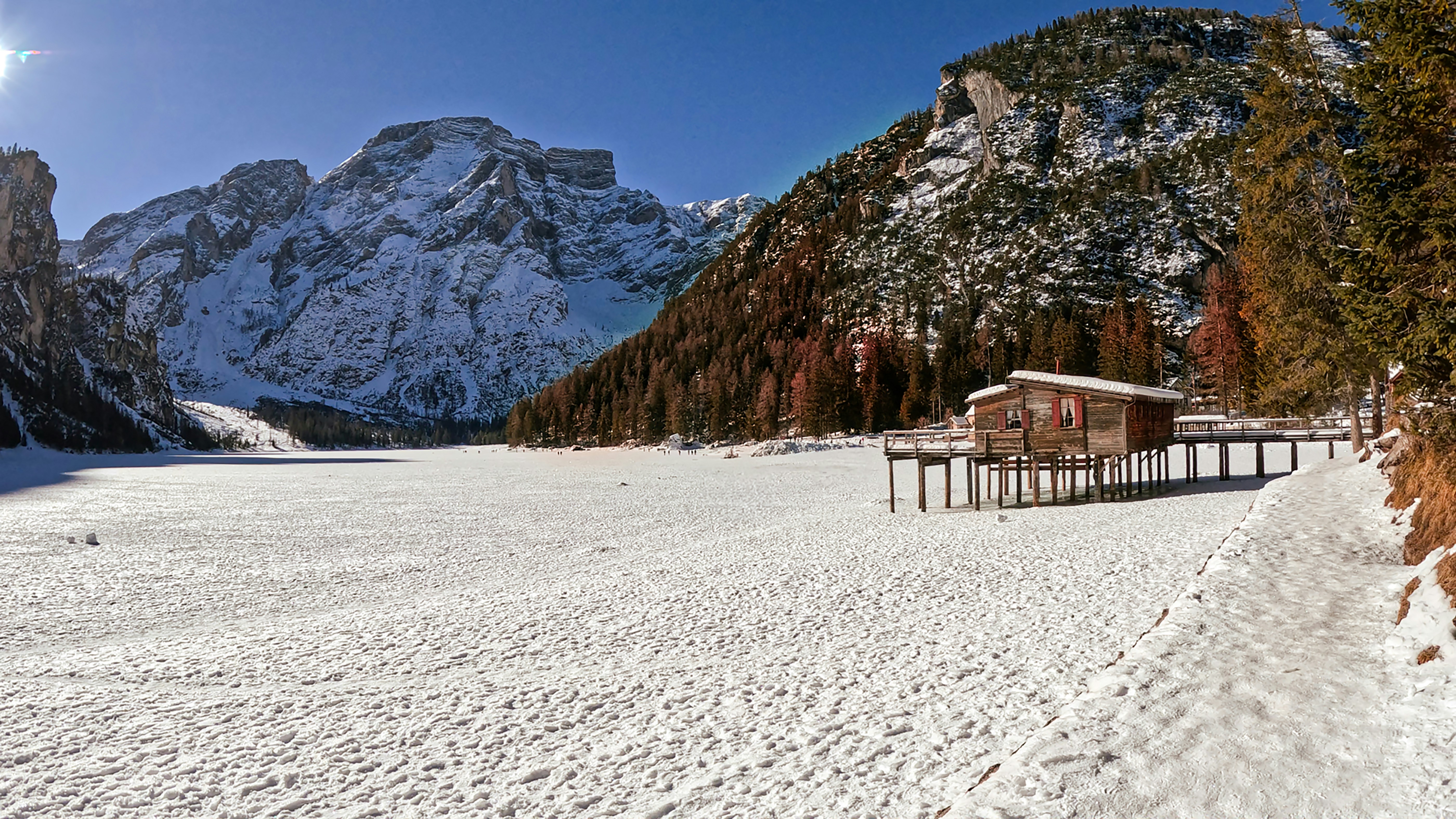 Snowy lake with mountains and a rustic cabin.