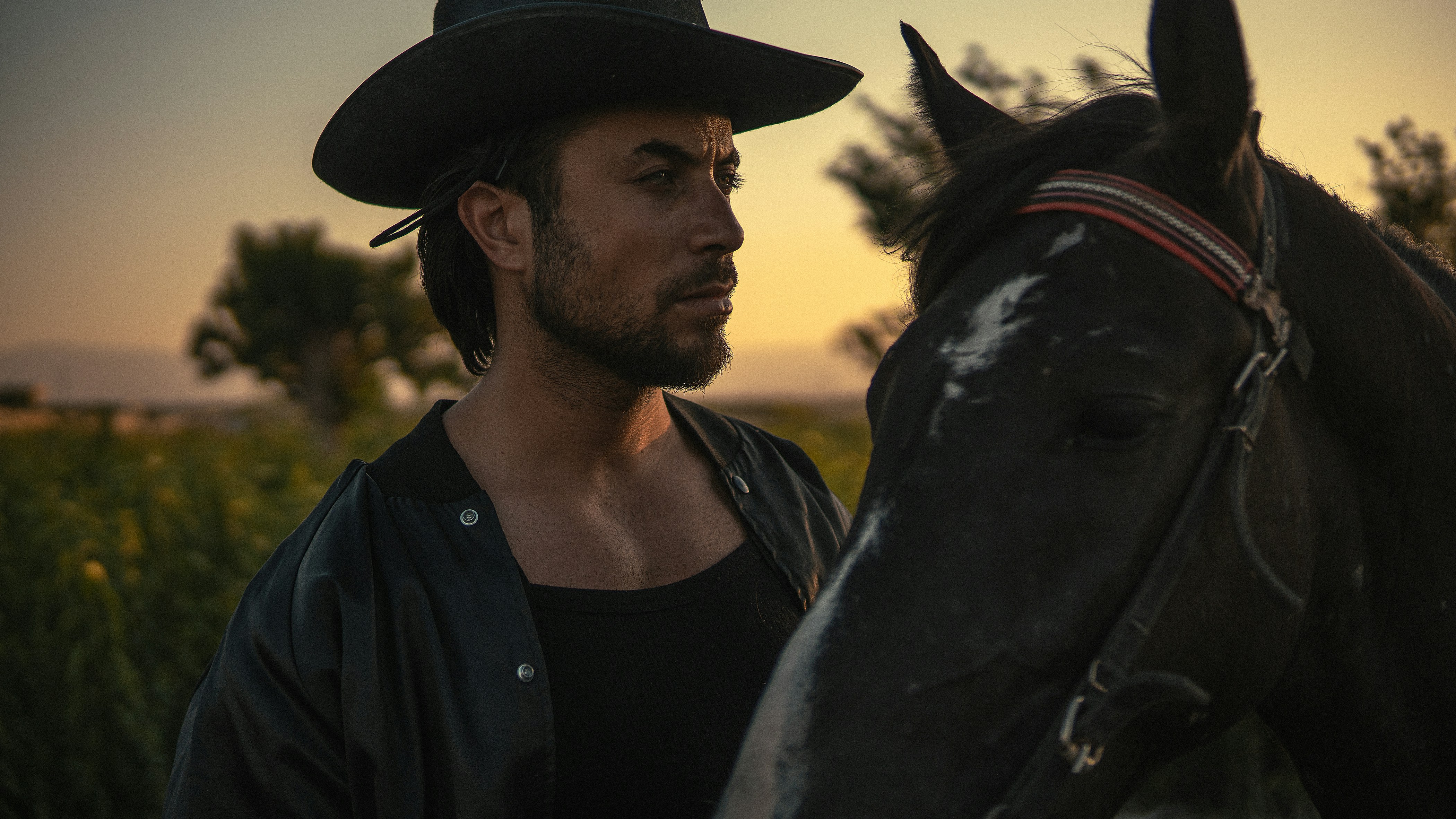 A cowboy stands beside his horse at sunset.