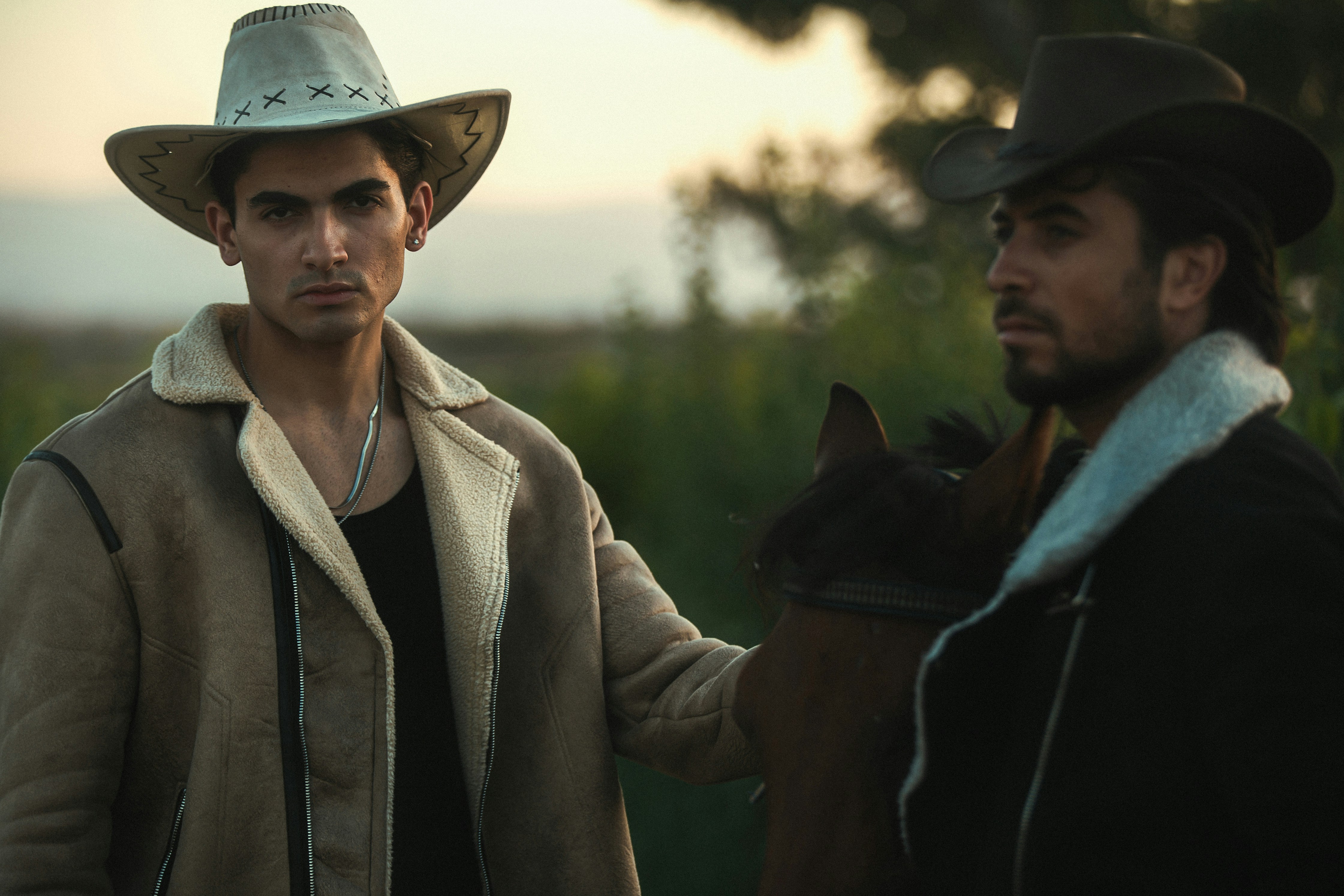Two cowboys stand together outdoors.