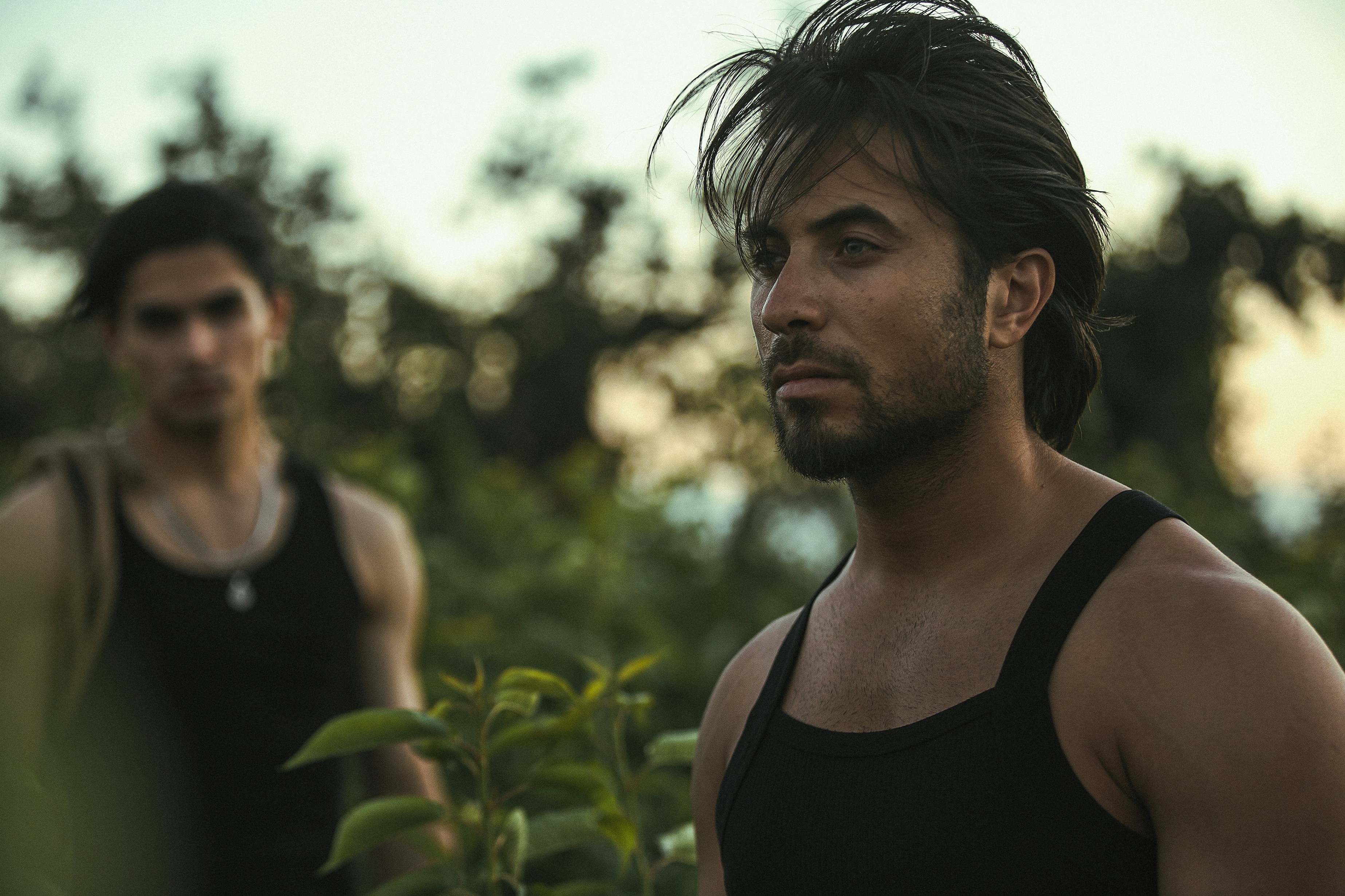 Two men stand in a field, one focused ahead.