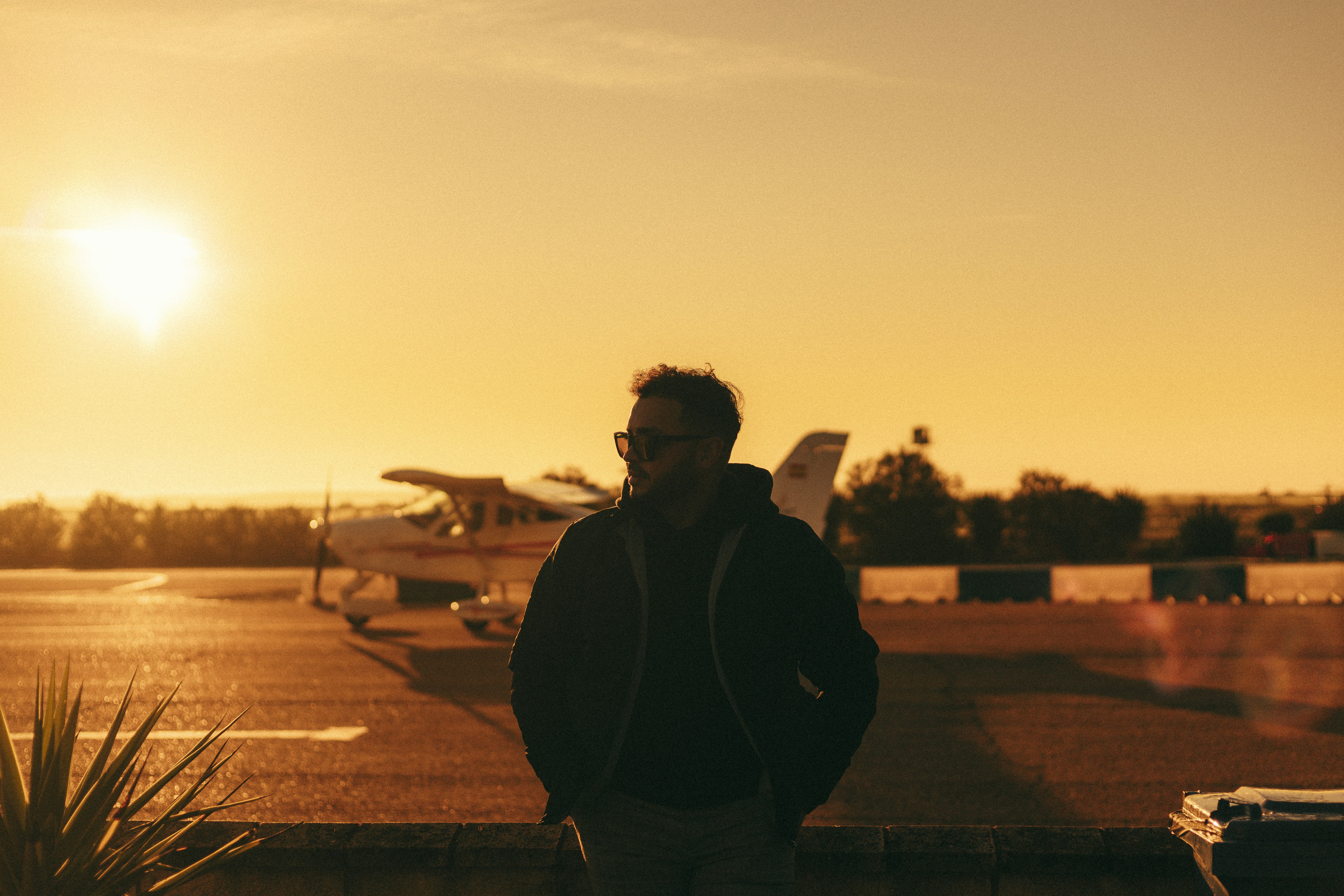 A man stands in front of a plane at sunset.