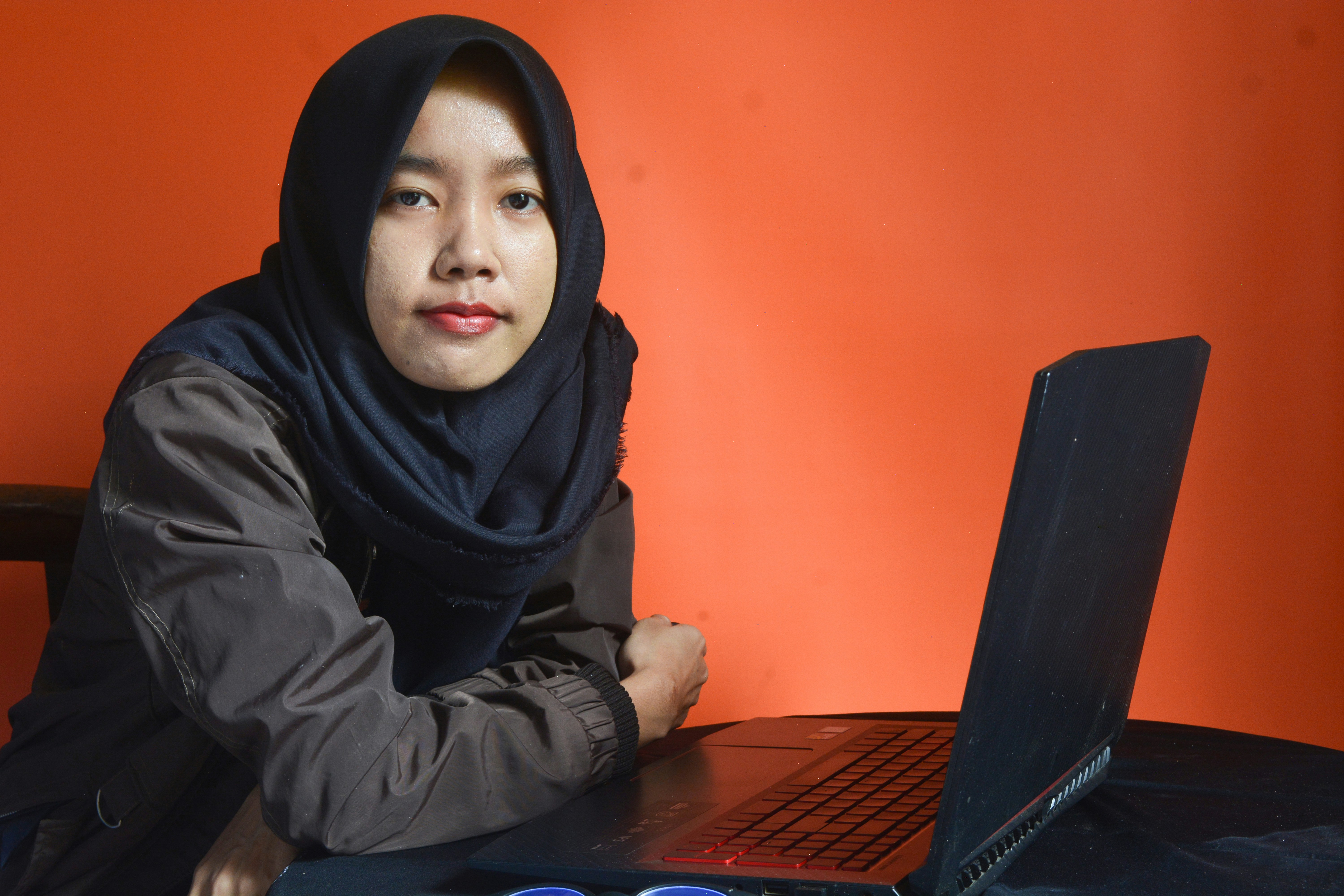 Portrait of smiling beautiful Asian woman in casual shirt and hijab holding a laptop and looking at camera isolated over white background. People religious lifestyle concept
