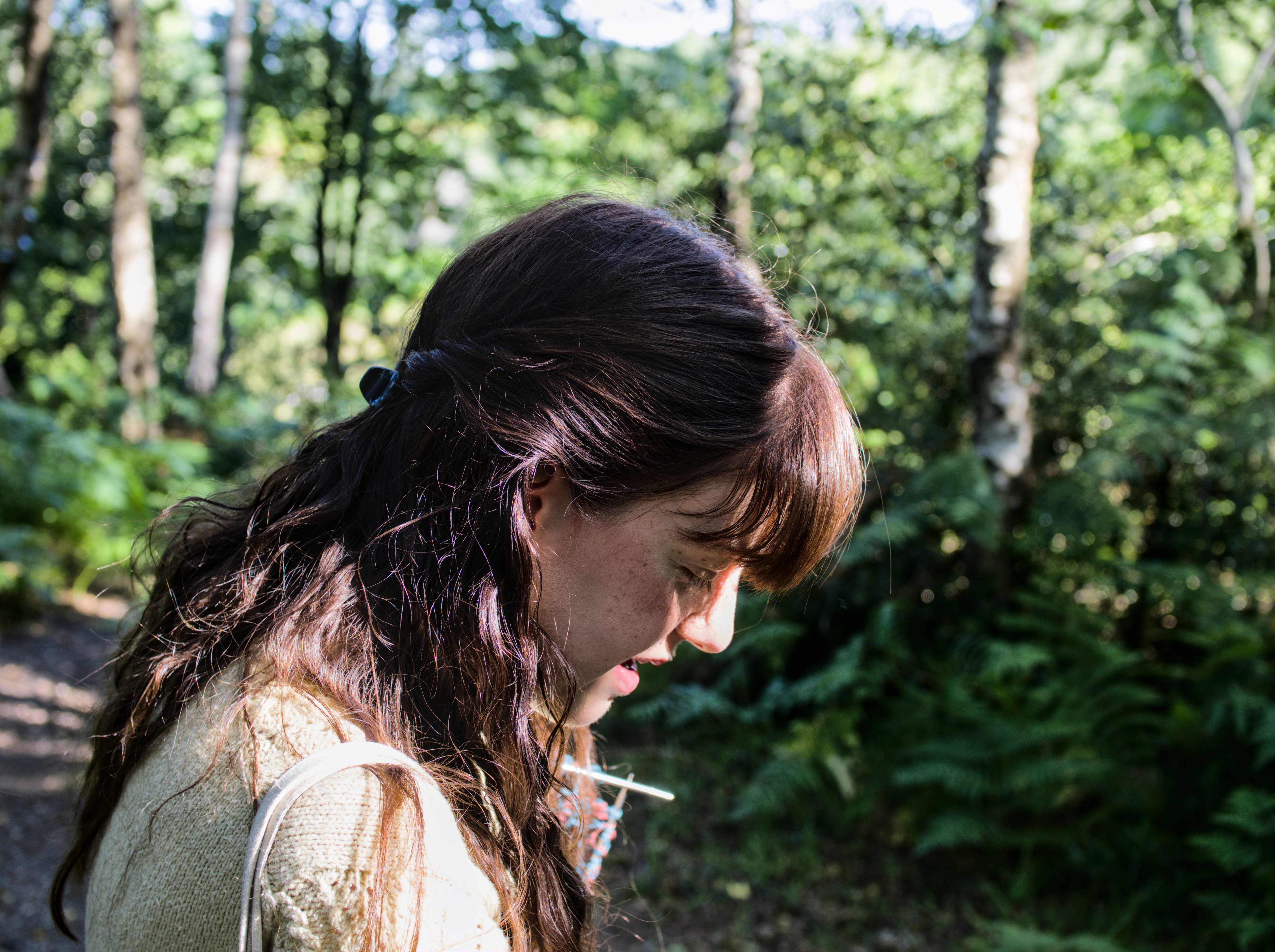 Woman in the woods looking down pensively.