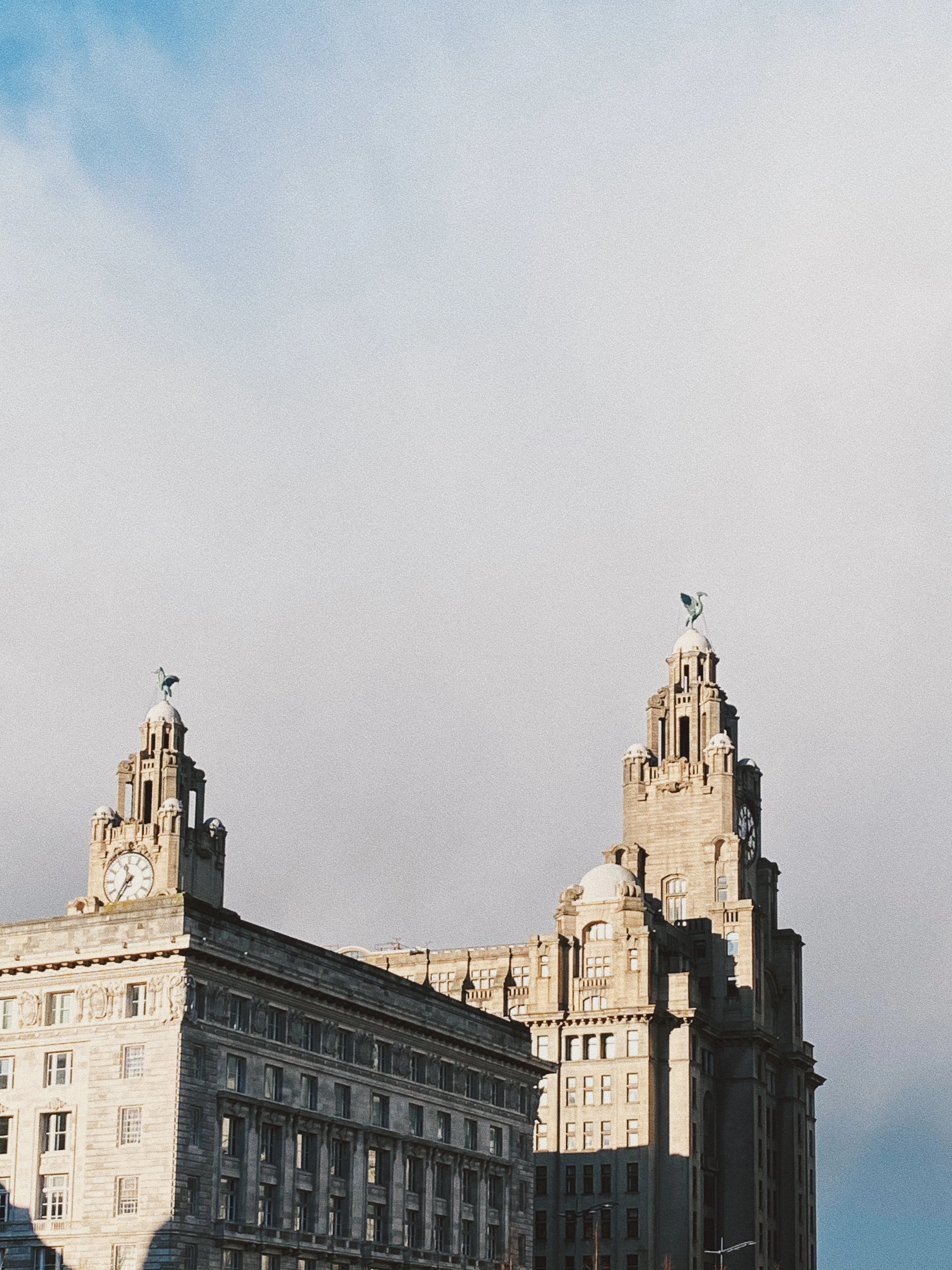 The twin clock towers of Liverpool's Royal Liver Building, each crowned by a Liver Bird, with the stone cornices of the neighbouring Cunard Building in the foreground