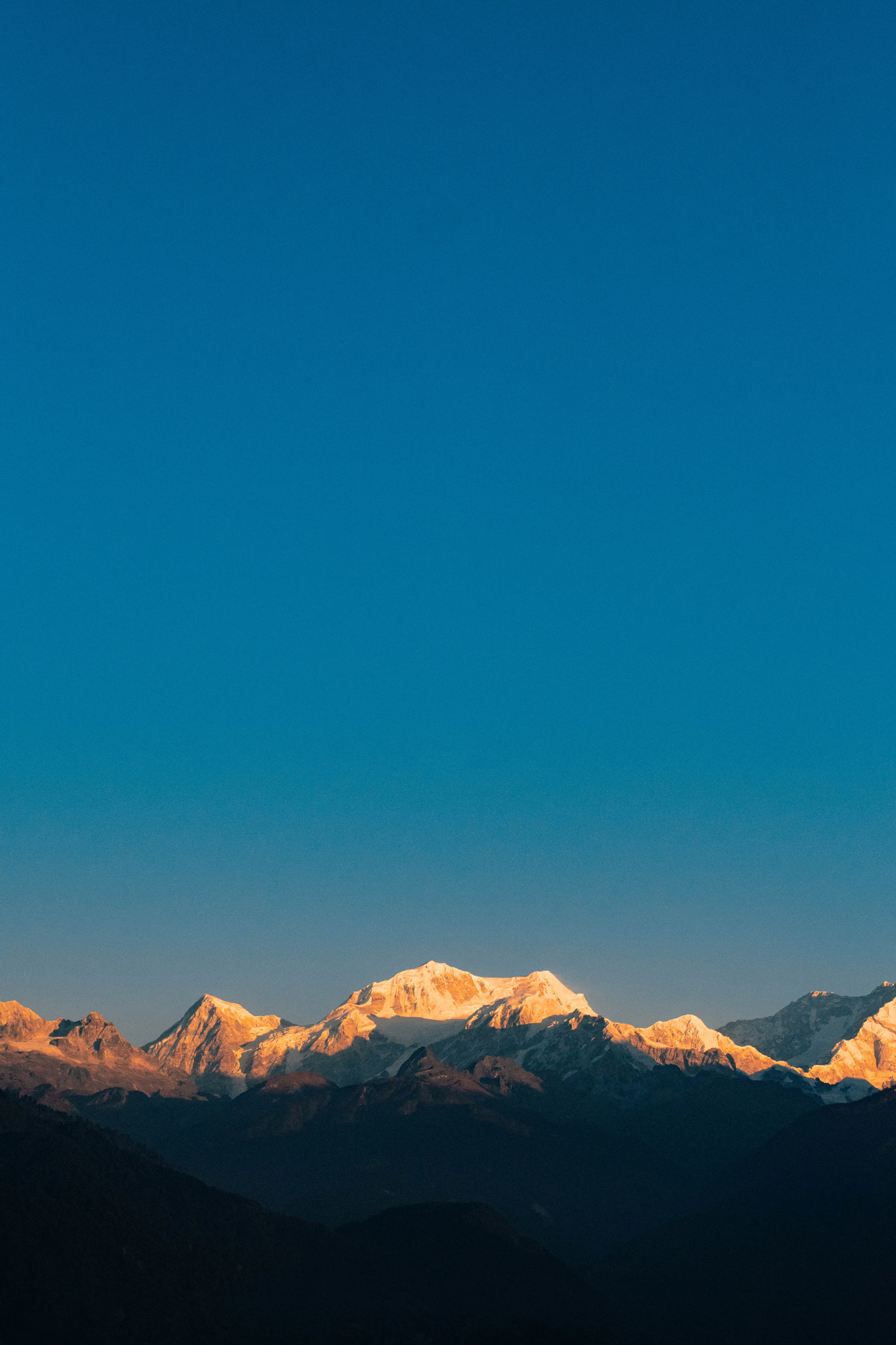 The Kanchenjunga range catching first sun above dark ridges, seen from Pelling under a clear deep blue dawn sky