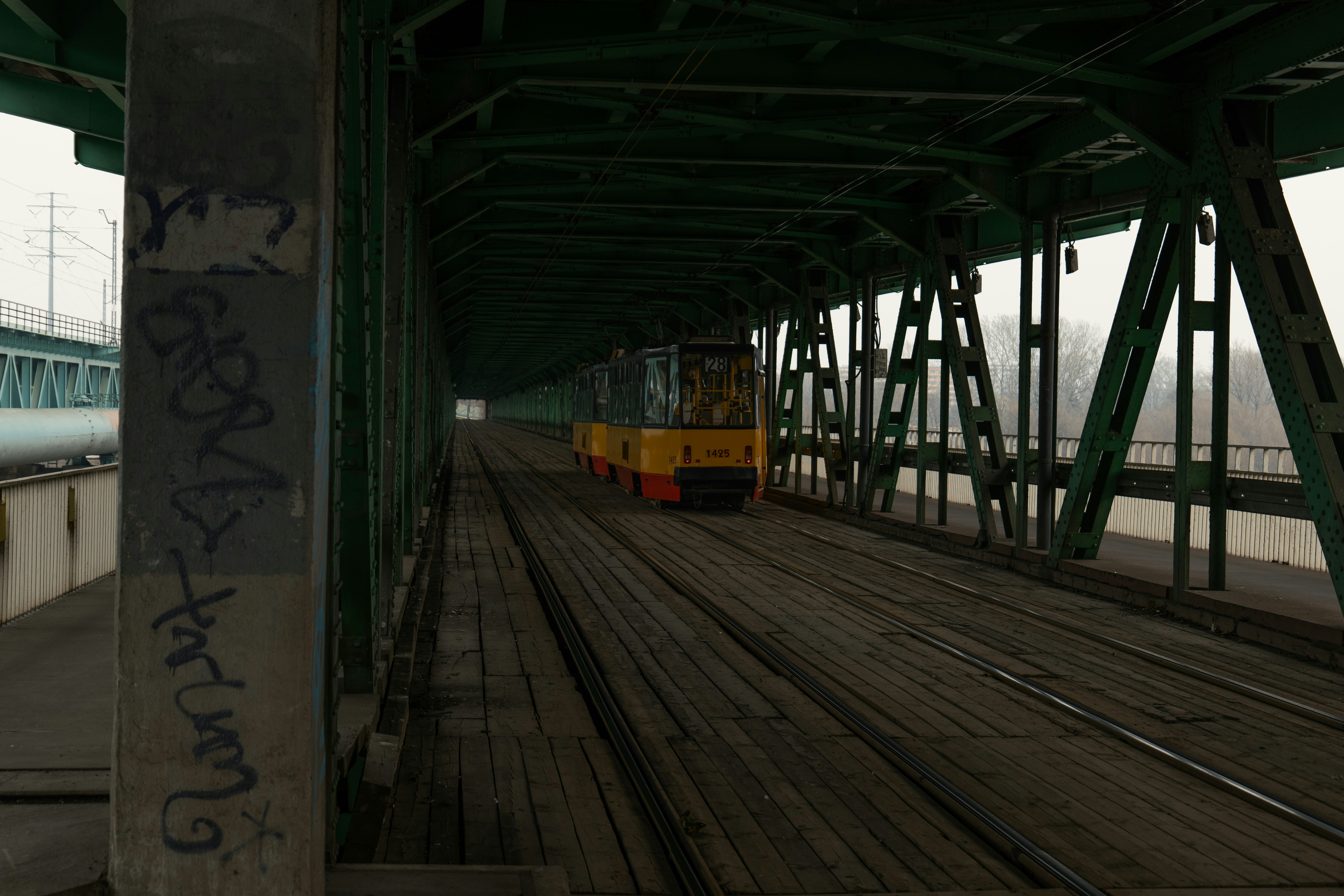A yellow tram travels across a metal bridge.