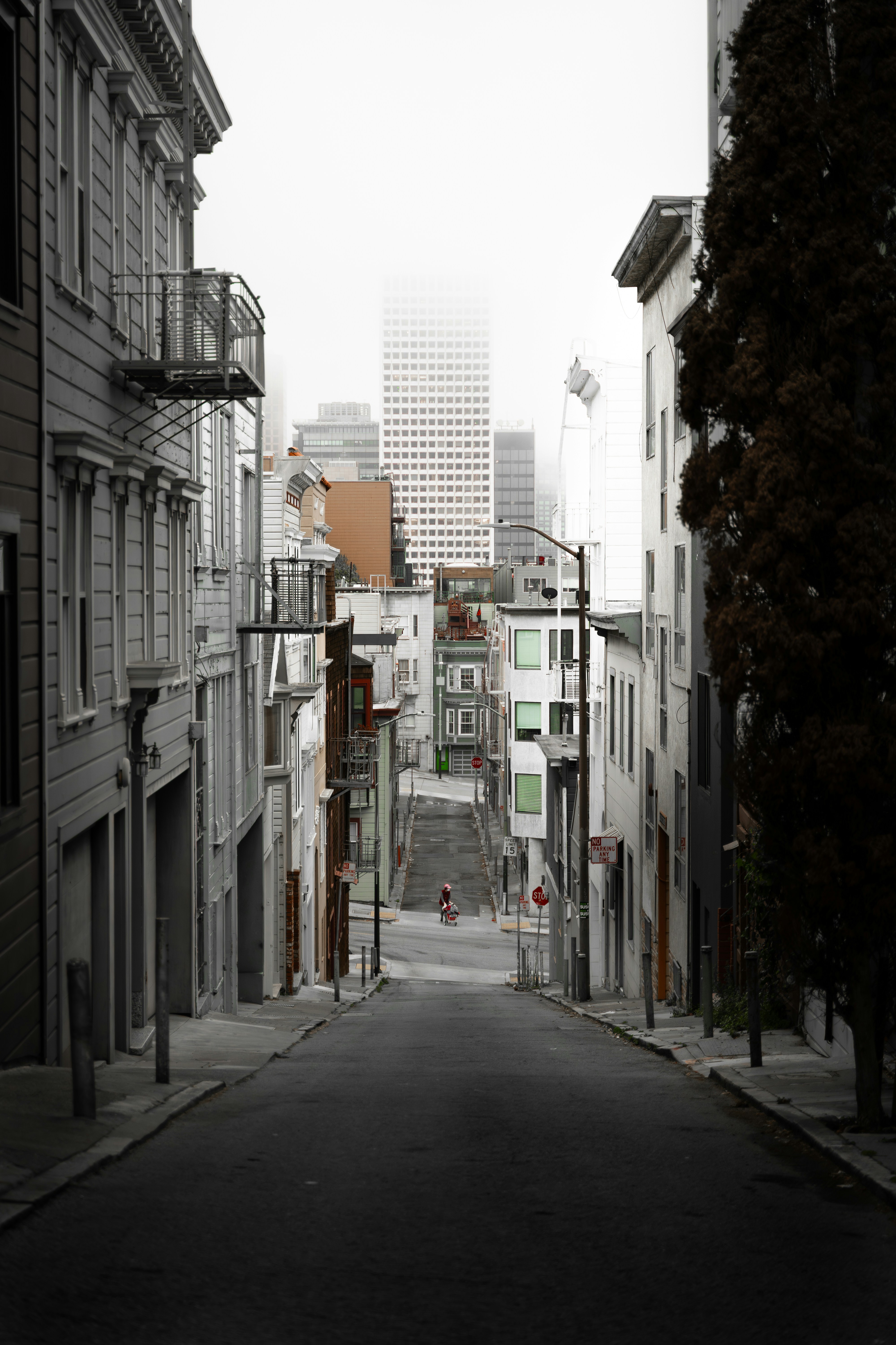 A steep city street leads toward foggy skyscrapers.