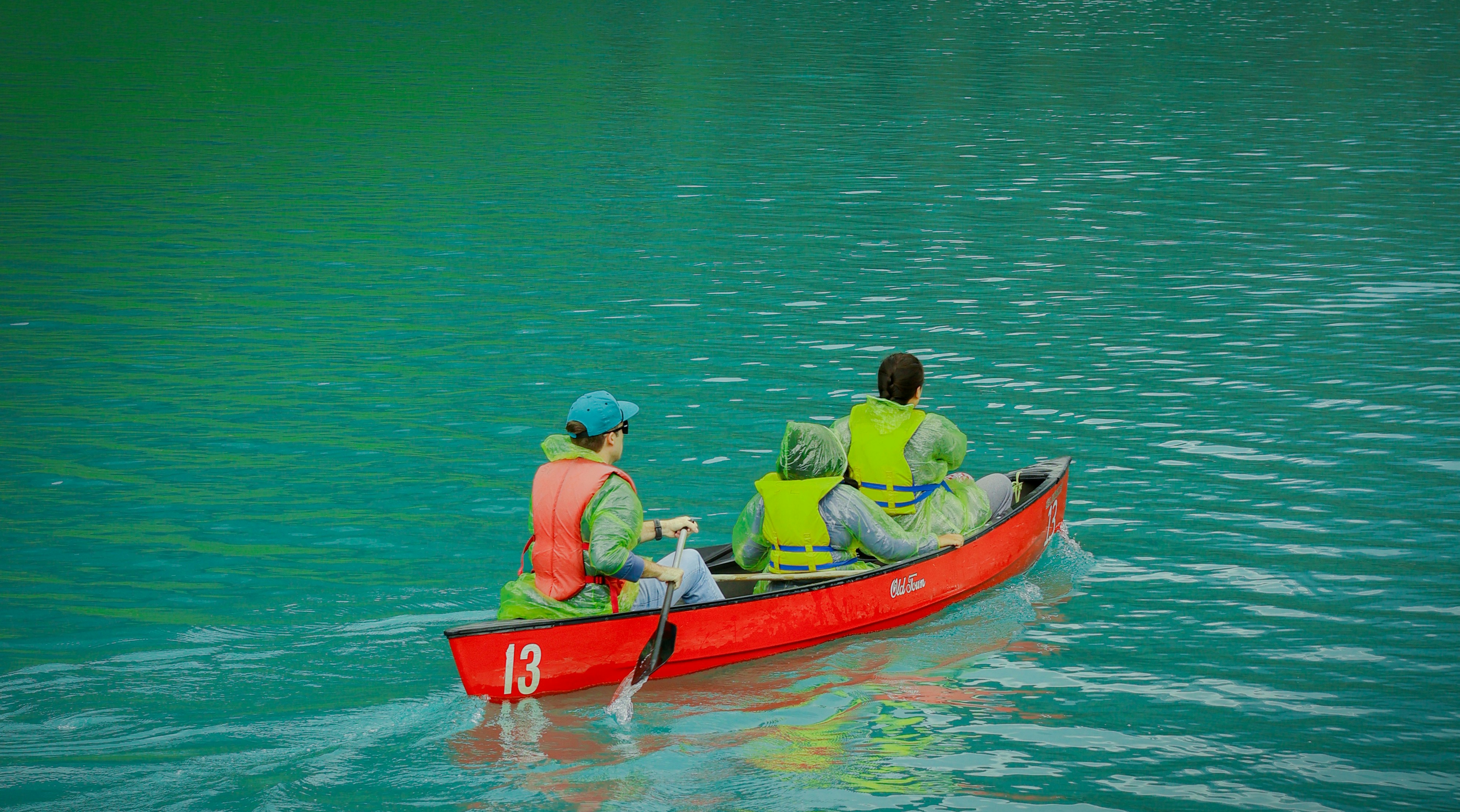 People paddle a canoe across a turquoise lake.