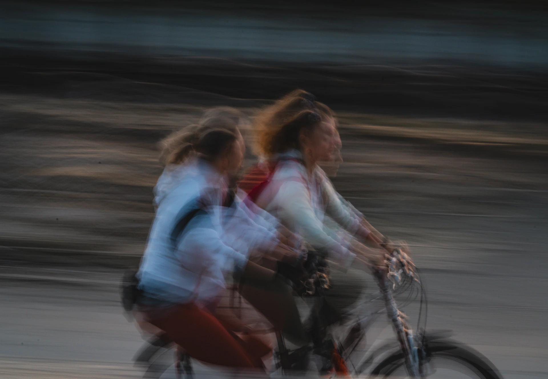 Two people bicycle together, blurred by speed.