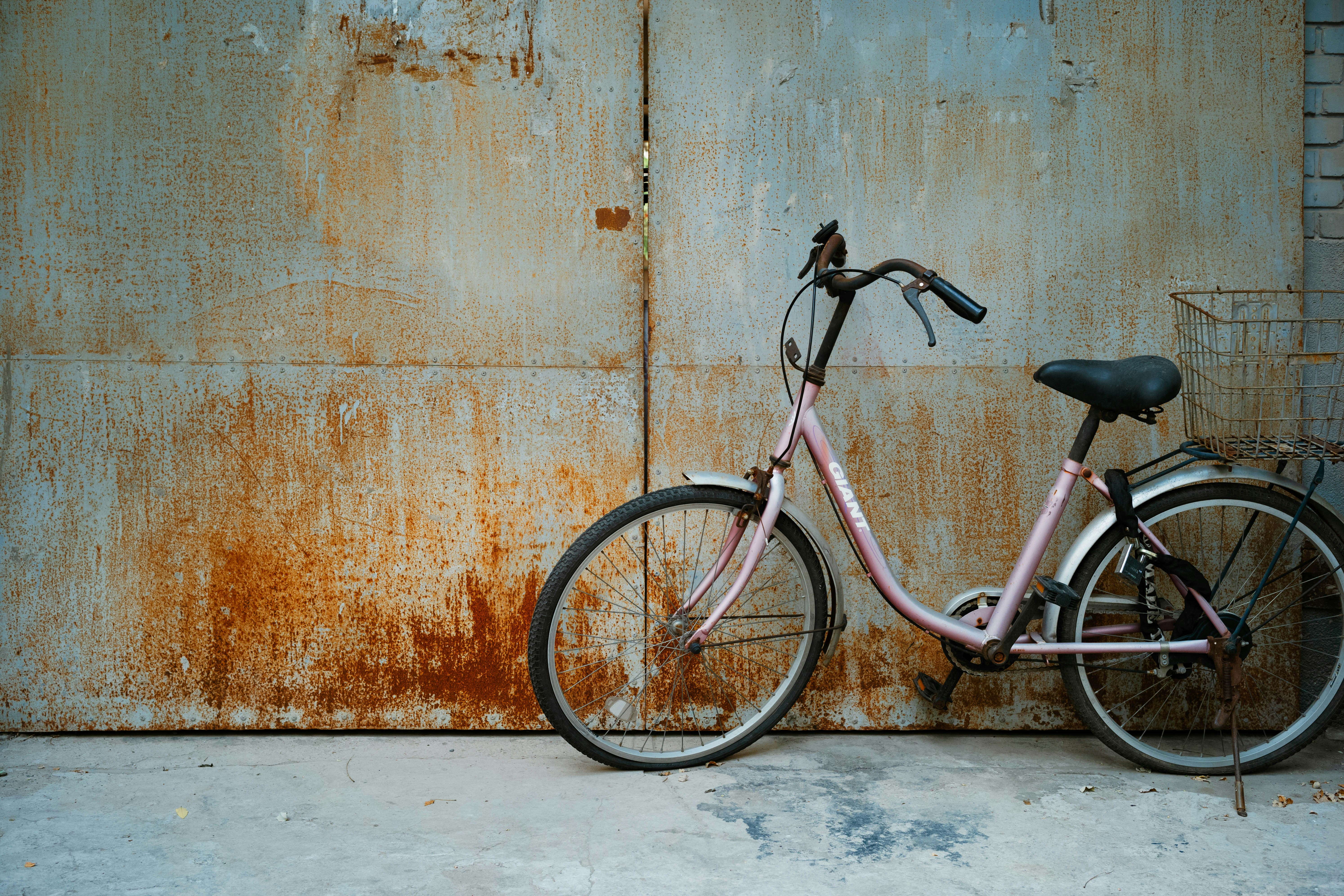 A pink bicycle leans against a rusty wall.
