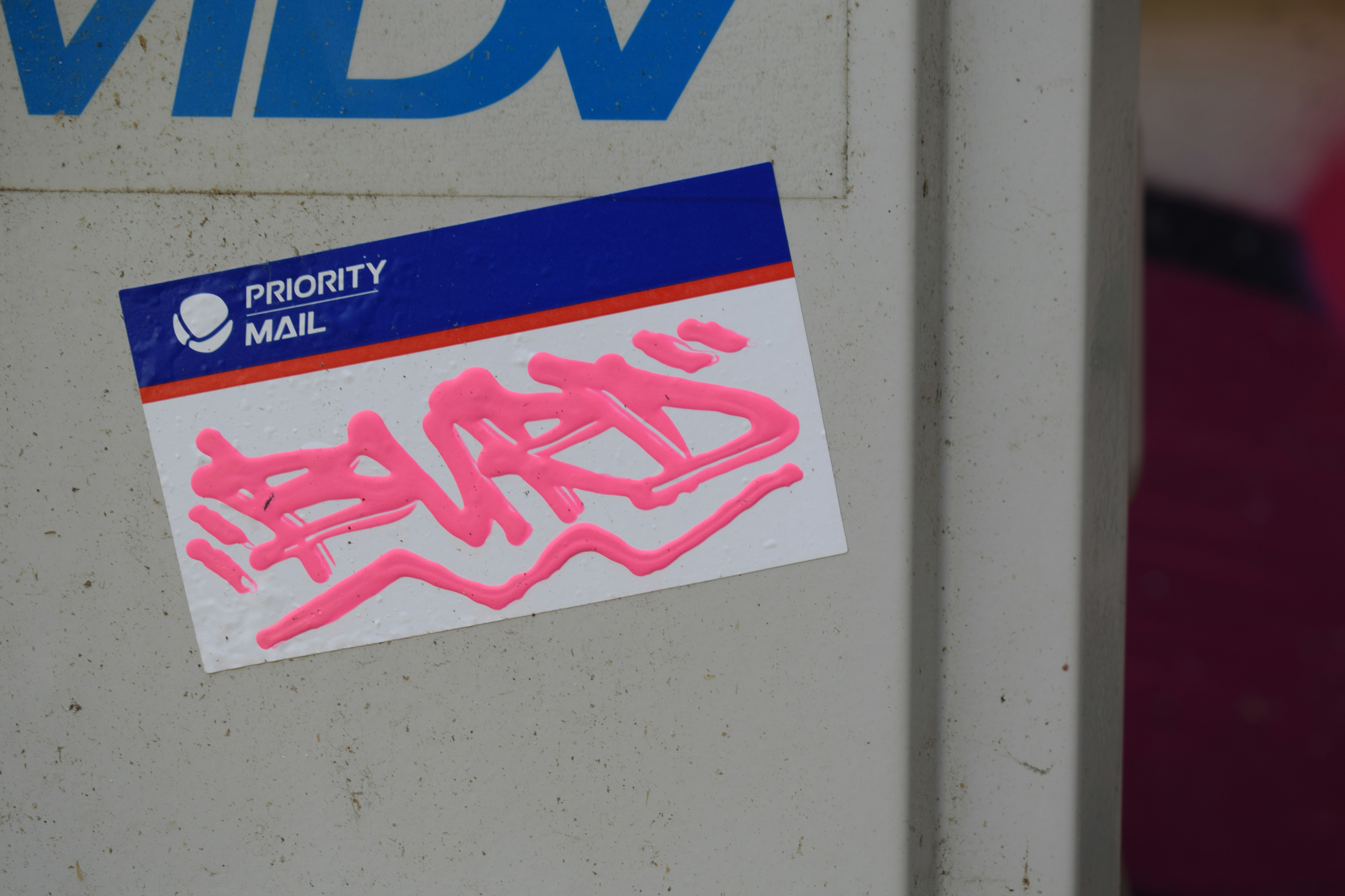 Pink graffiti is displayed on a priority mail sticker.