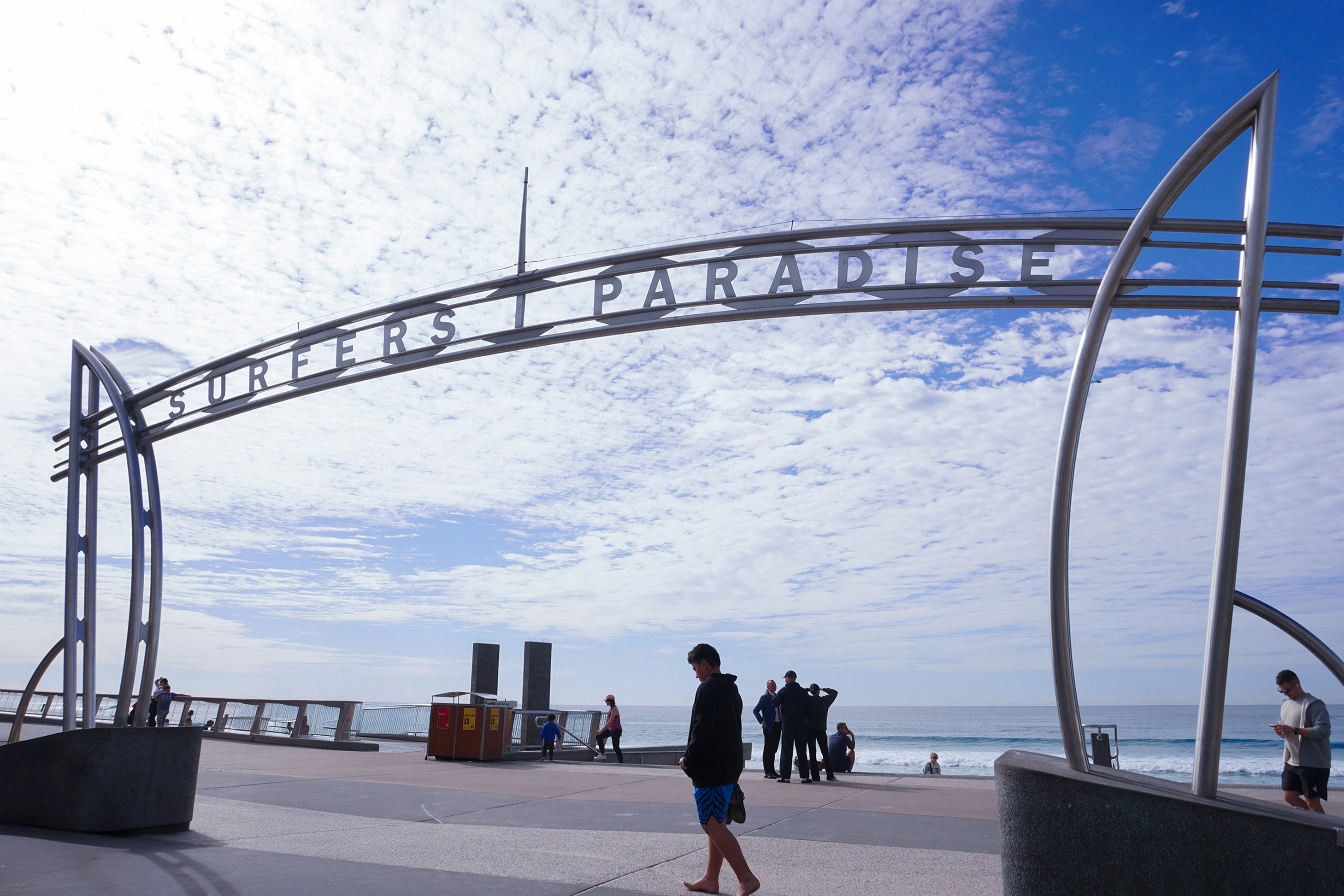 Surfers paradise sign stands with people and a blue sky.
