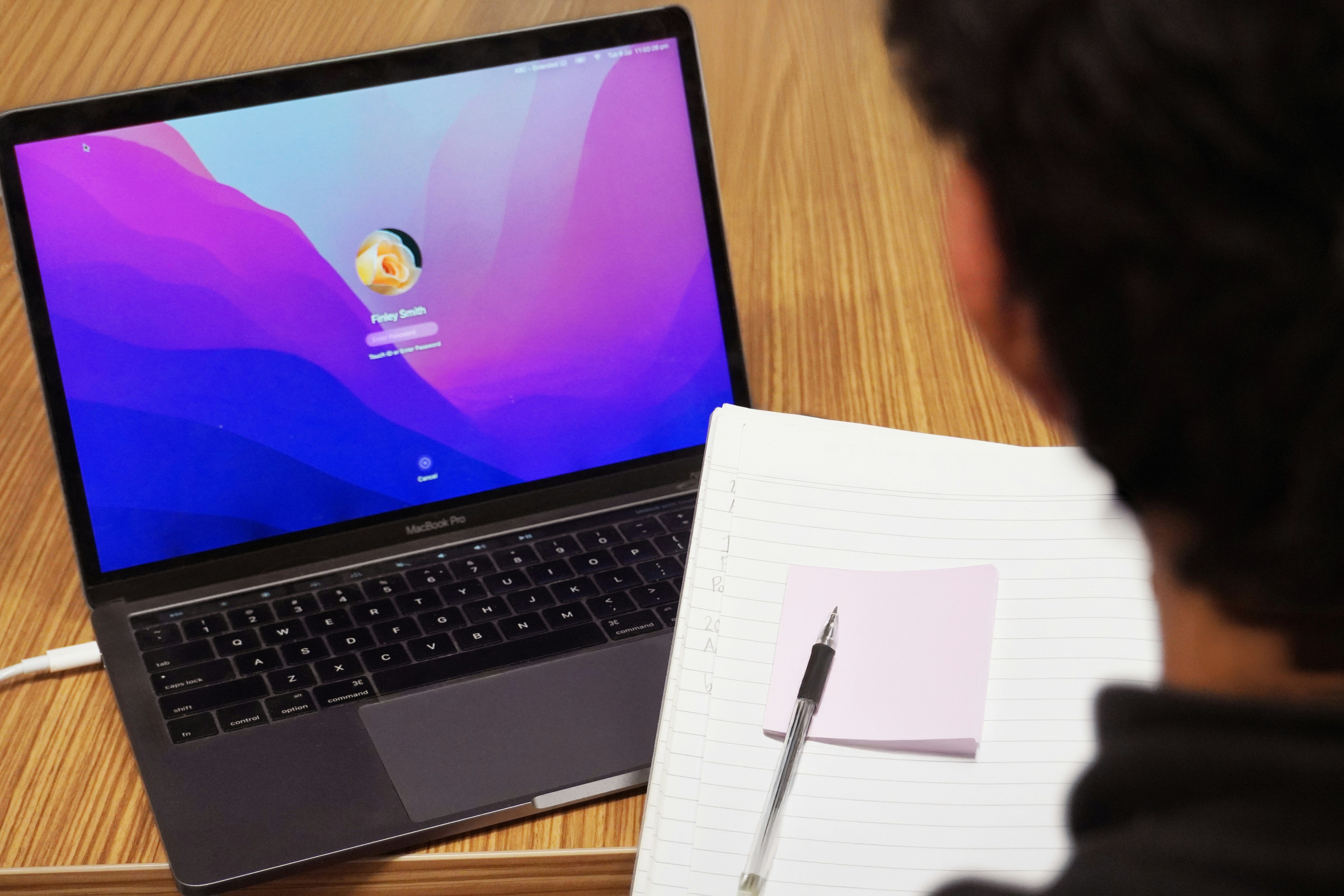 Orang yang menggunakan laptop dengan notebook dan pena.