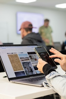 Person using phone and laptop in a workspace.