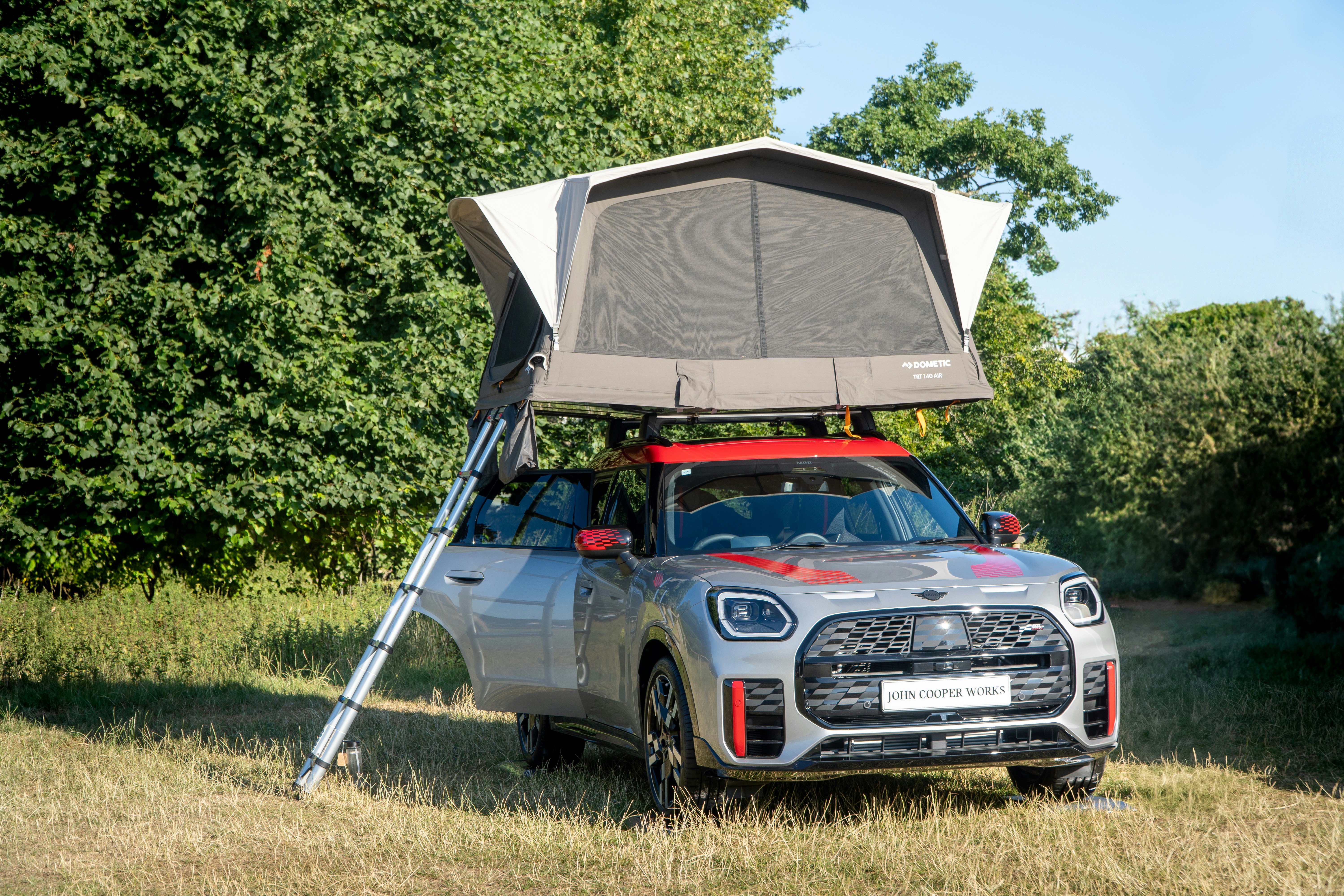 A car with a rooftop tent pitched on a grassy field.