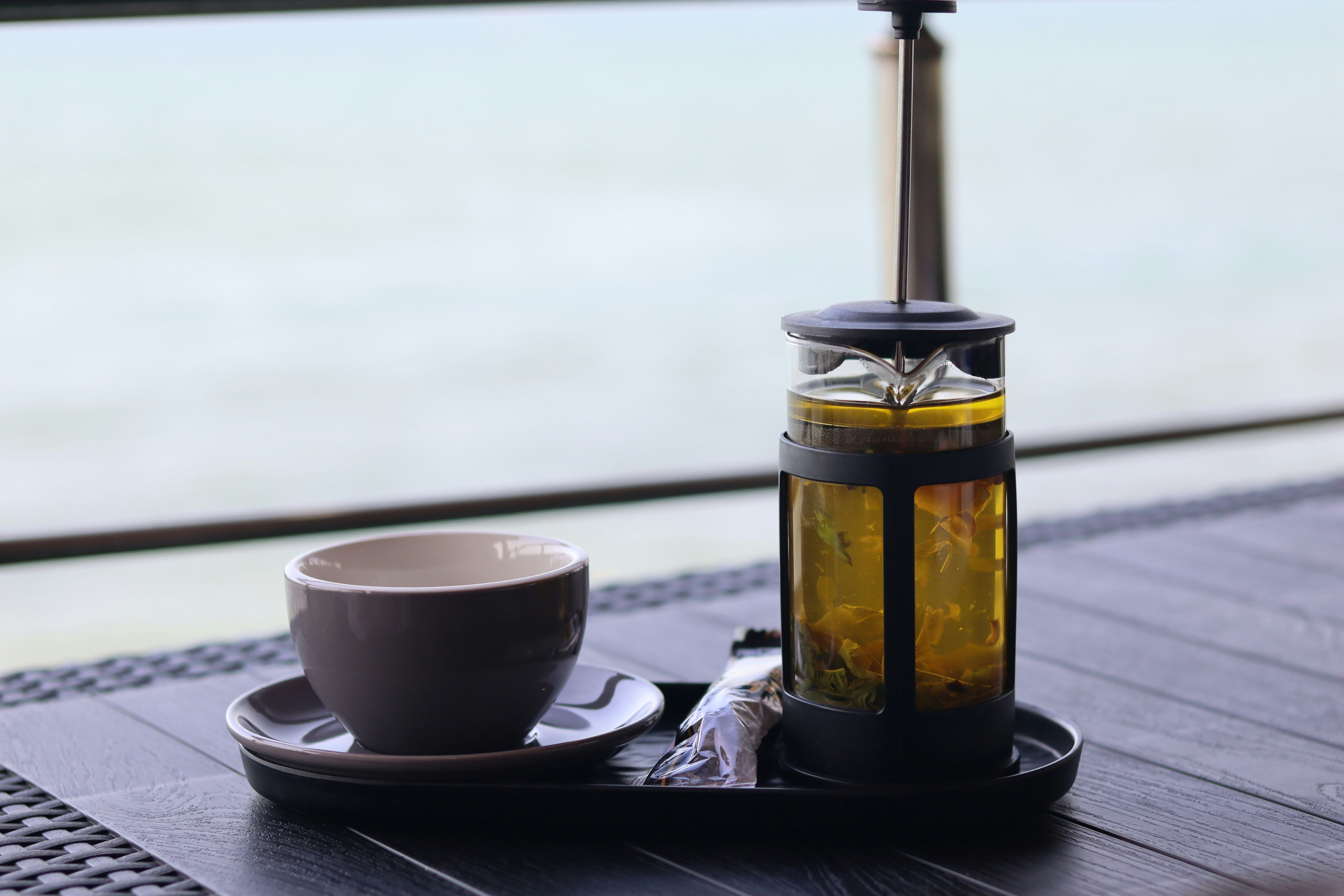Tea and a cup sit on a table by the water.