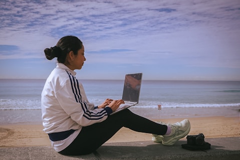 Woman works on laptop by the beach.