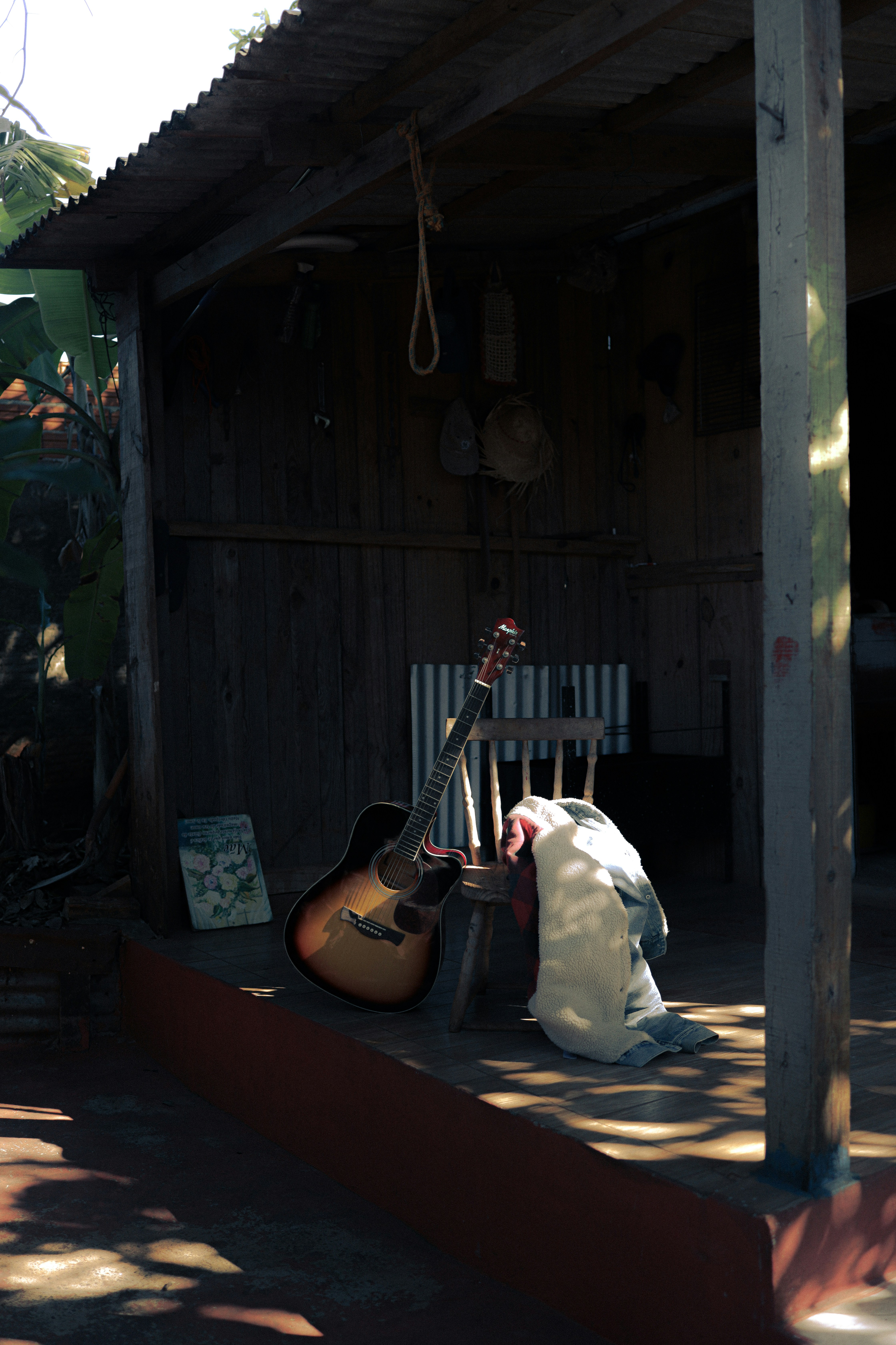 Une guitare repose à côté d’une chaise sous un cabanon.