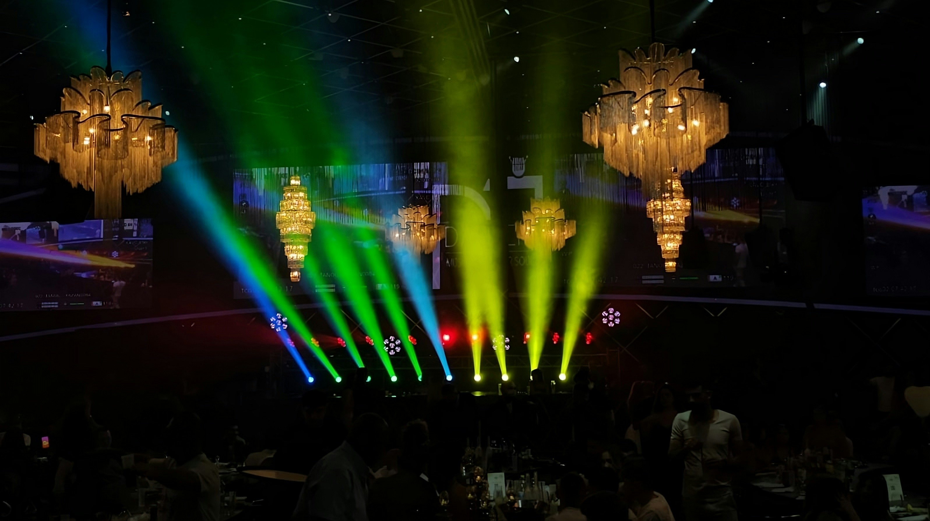Stage lights illuminate an event with chandeliers
