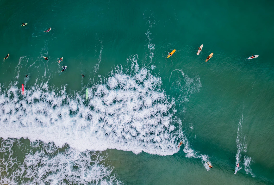Aerial view of paddleboarders and surfers in blue ocean waves