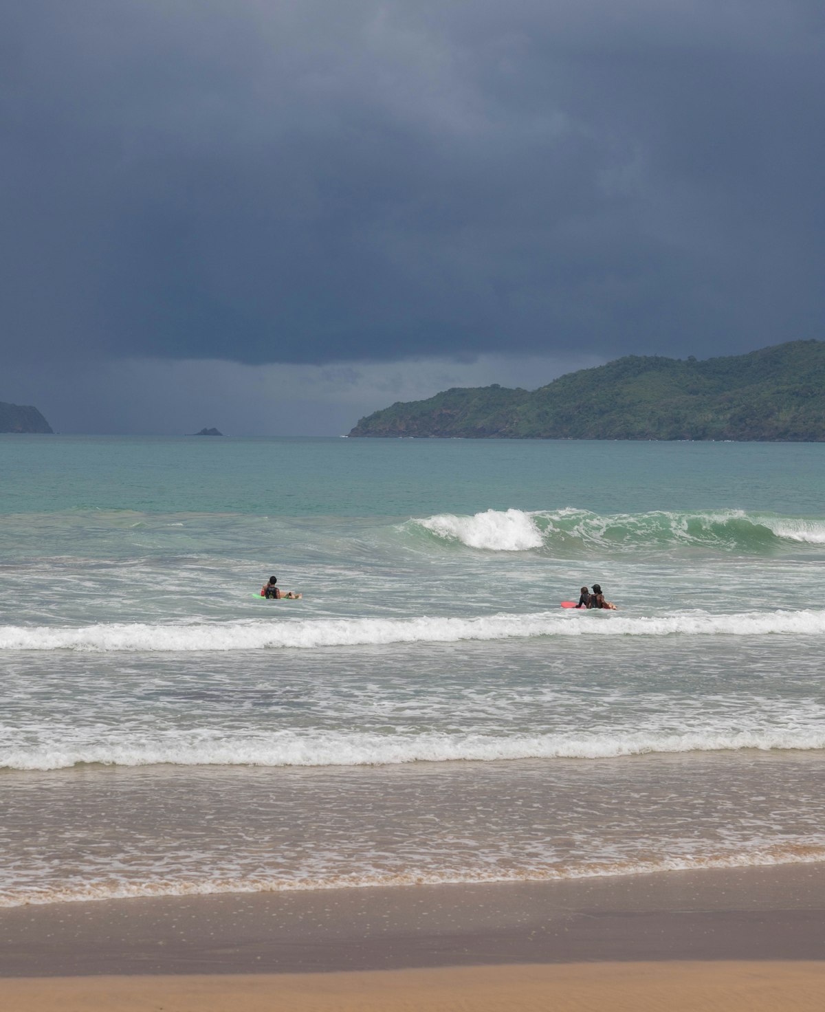 Phuket July — surfers riding waves under a dark dramatic monsoon storm sky