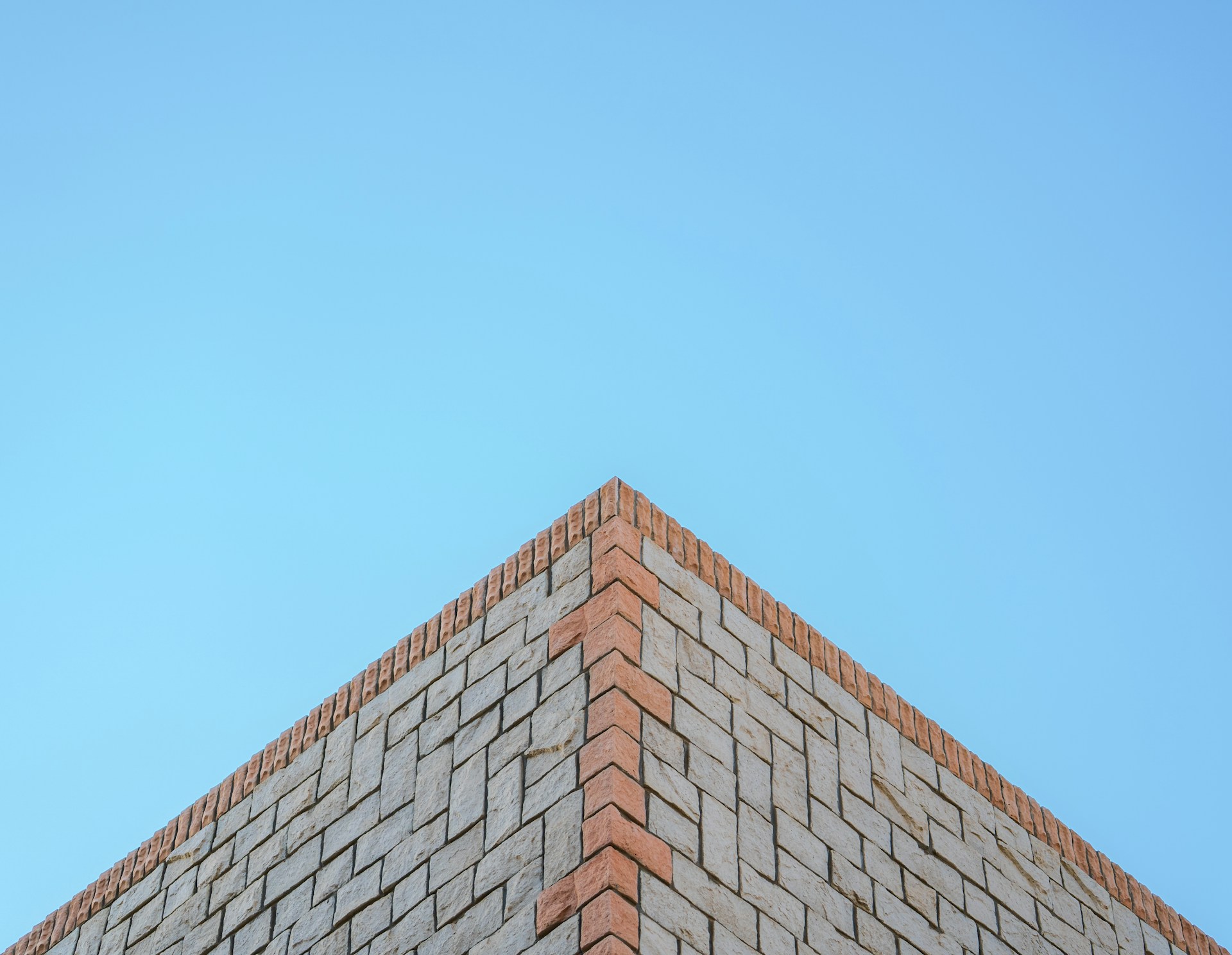A brick wall's corner meets the blue sky.