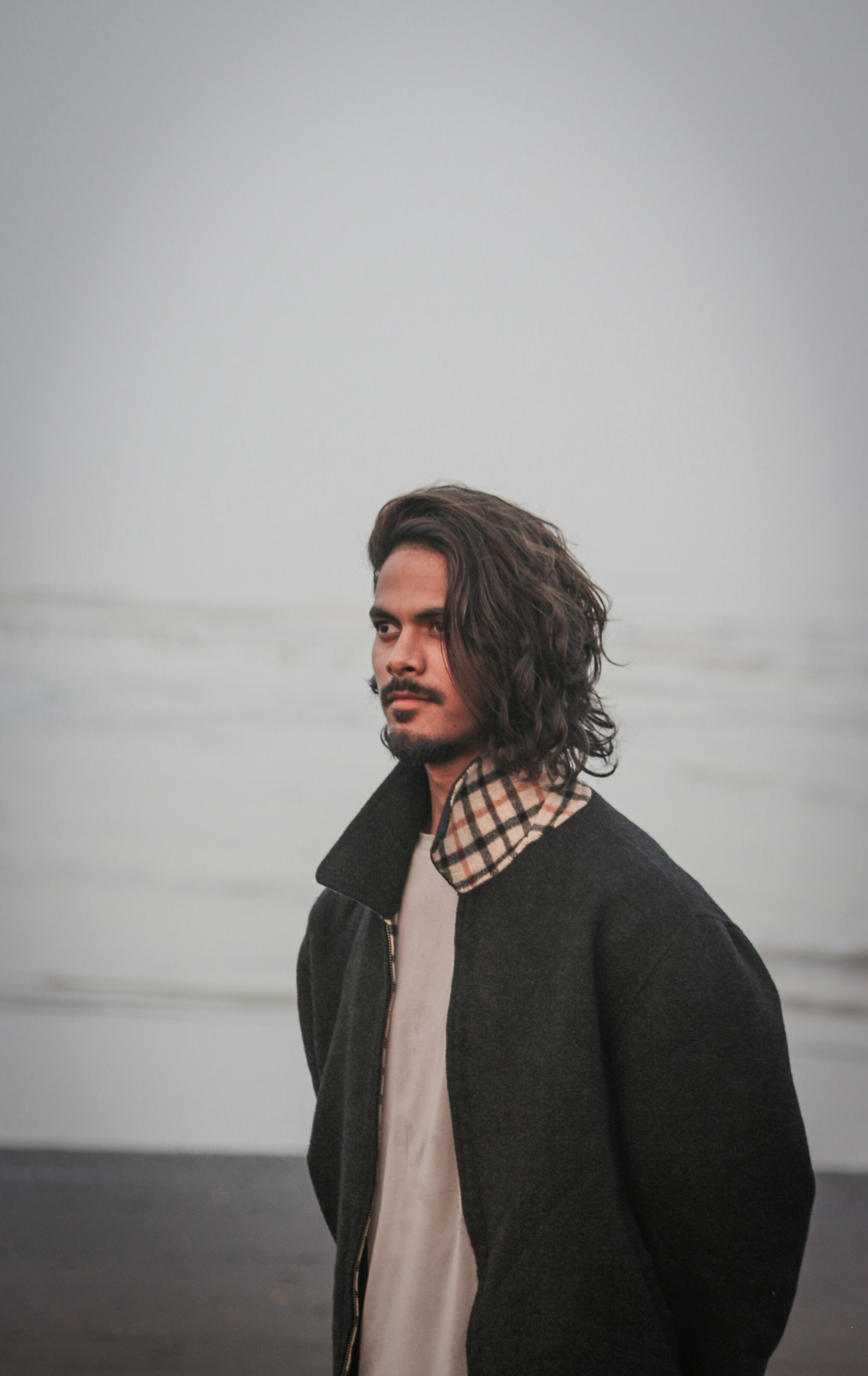 A man stands on a beach, looking thoughtful.