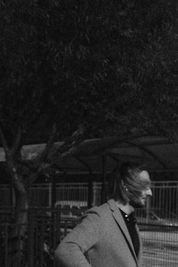 Man walks by a tree, hair blowing.