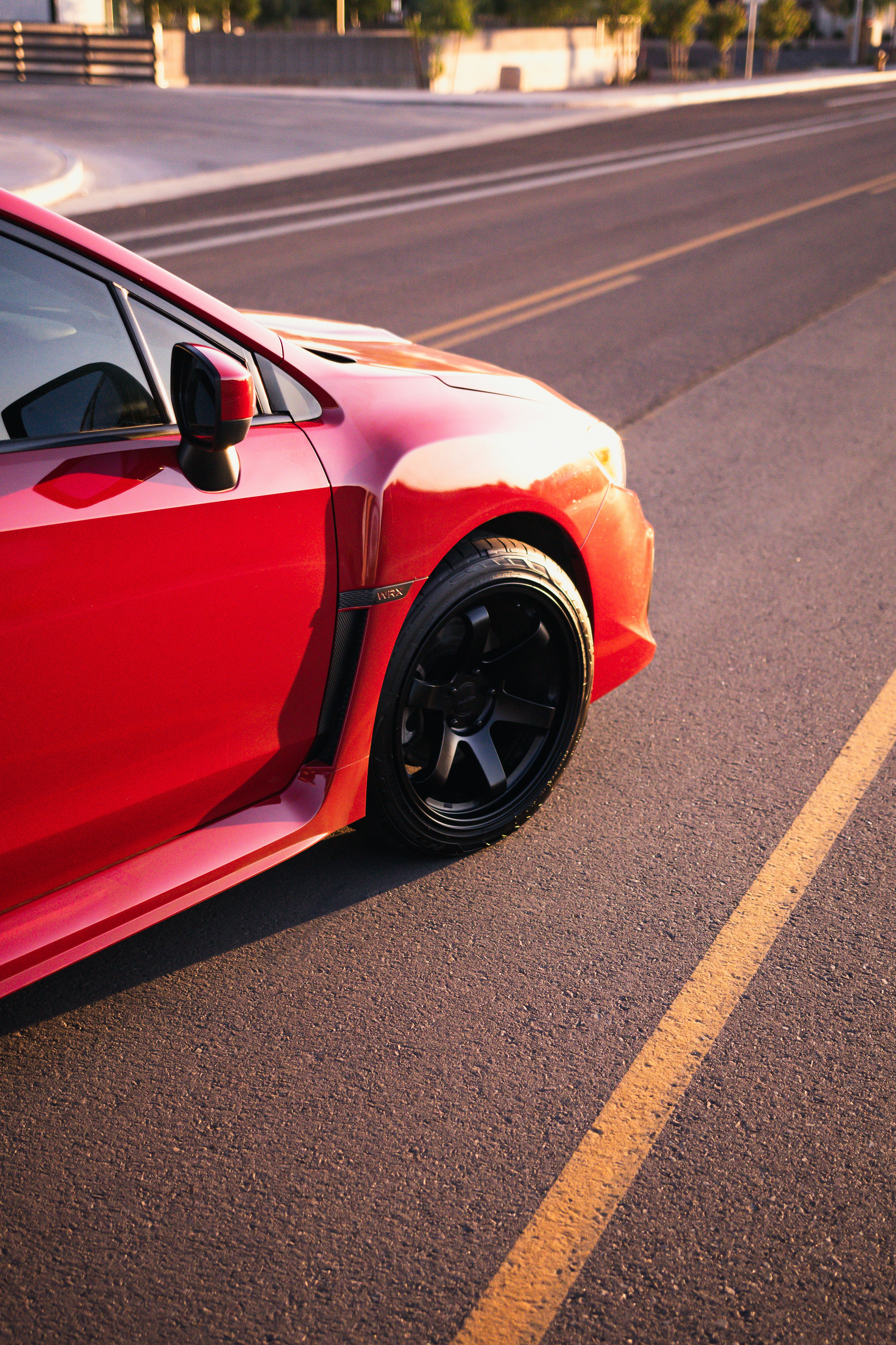 A red car is parked on a sunny road.