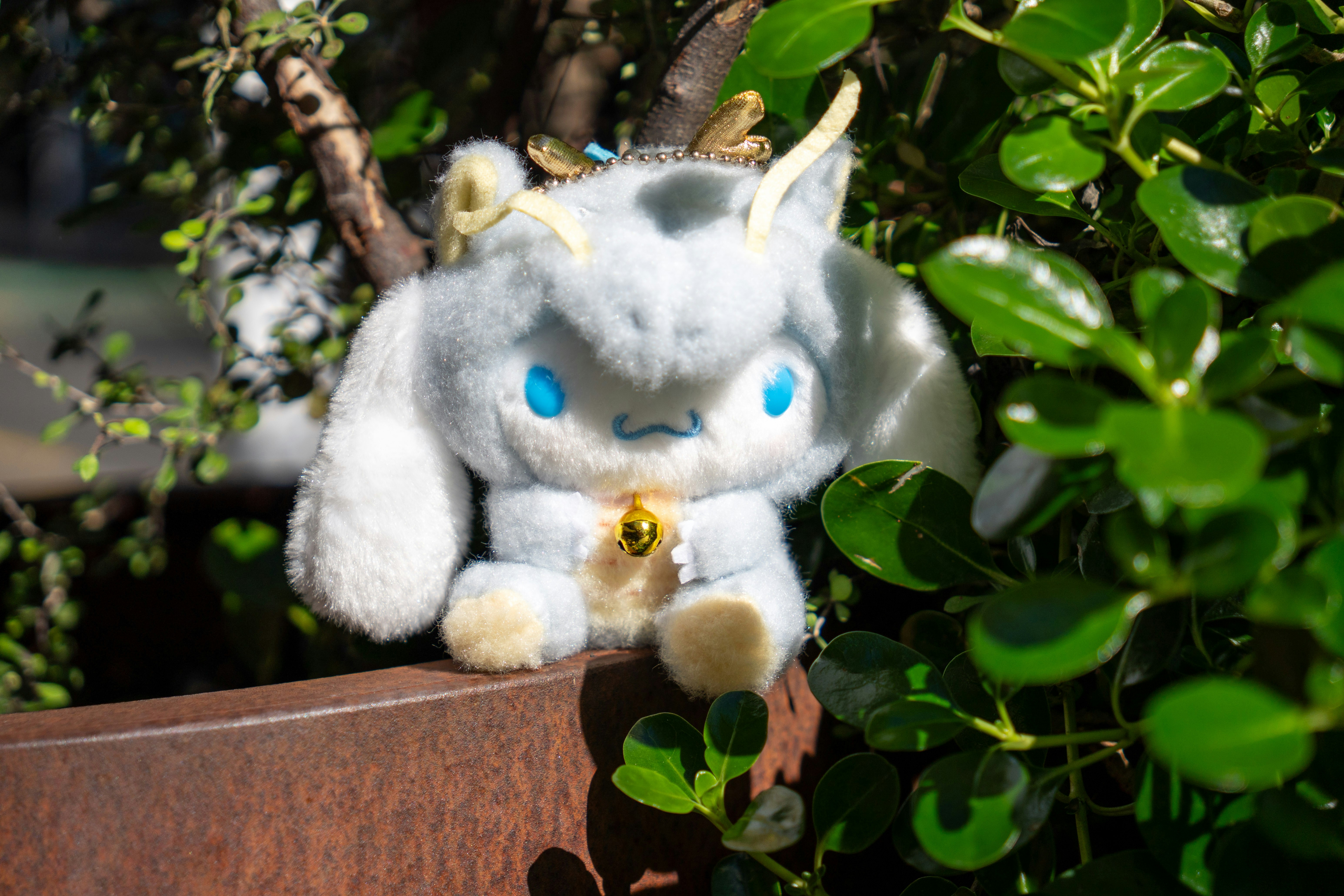 A cute plush dragon hides amongst green leaves.