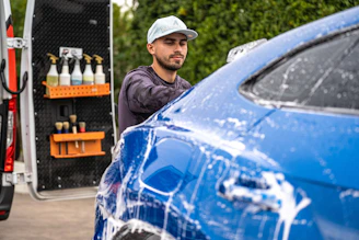 A man washes a blue car with soap.