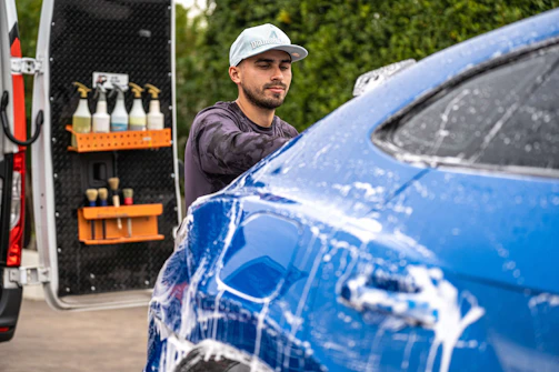 A man washes a blue car with soap
