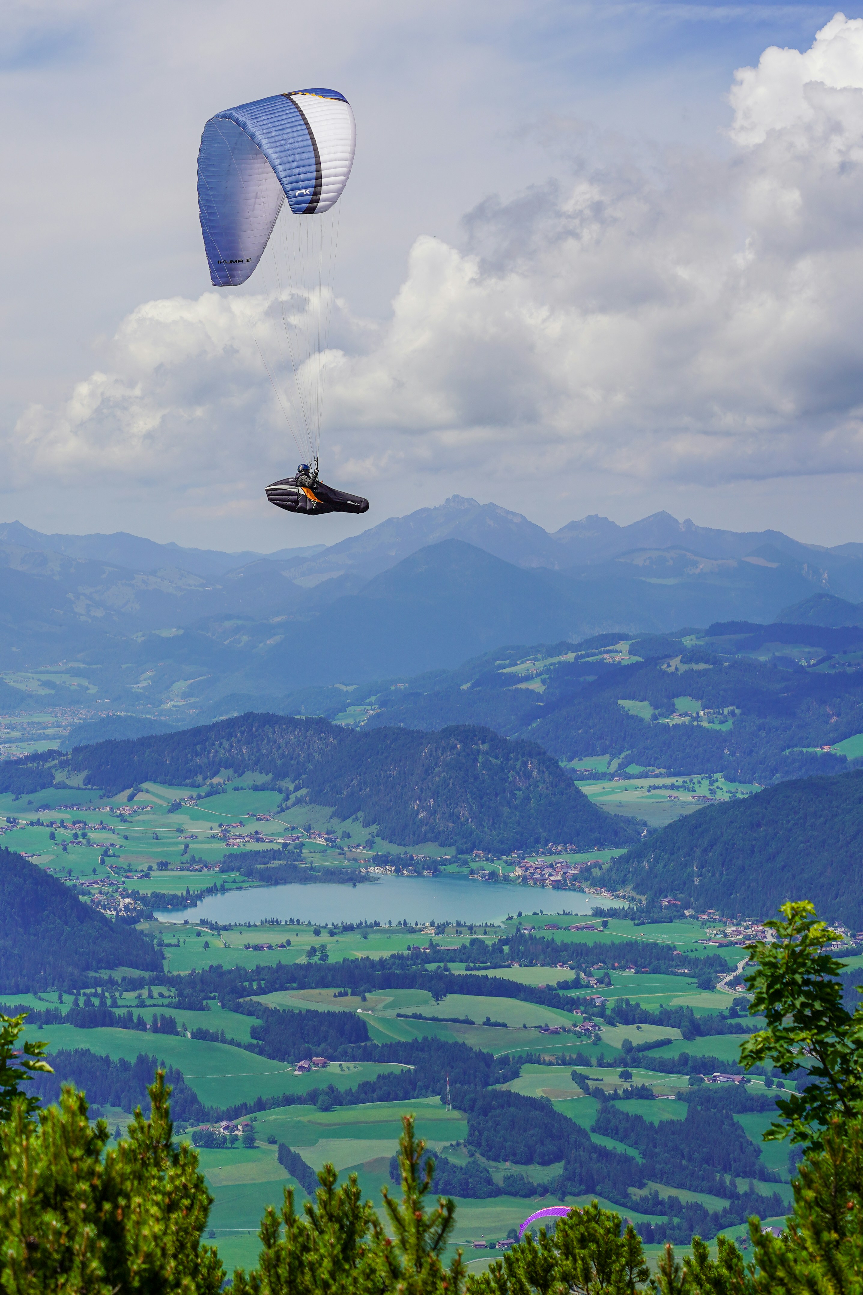 Paragliders soar over a scenic mountain landscape.