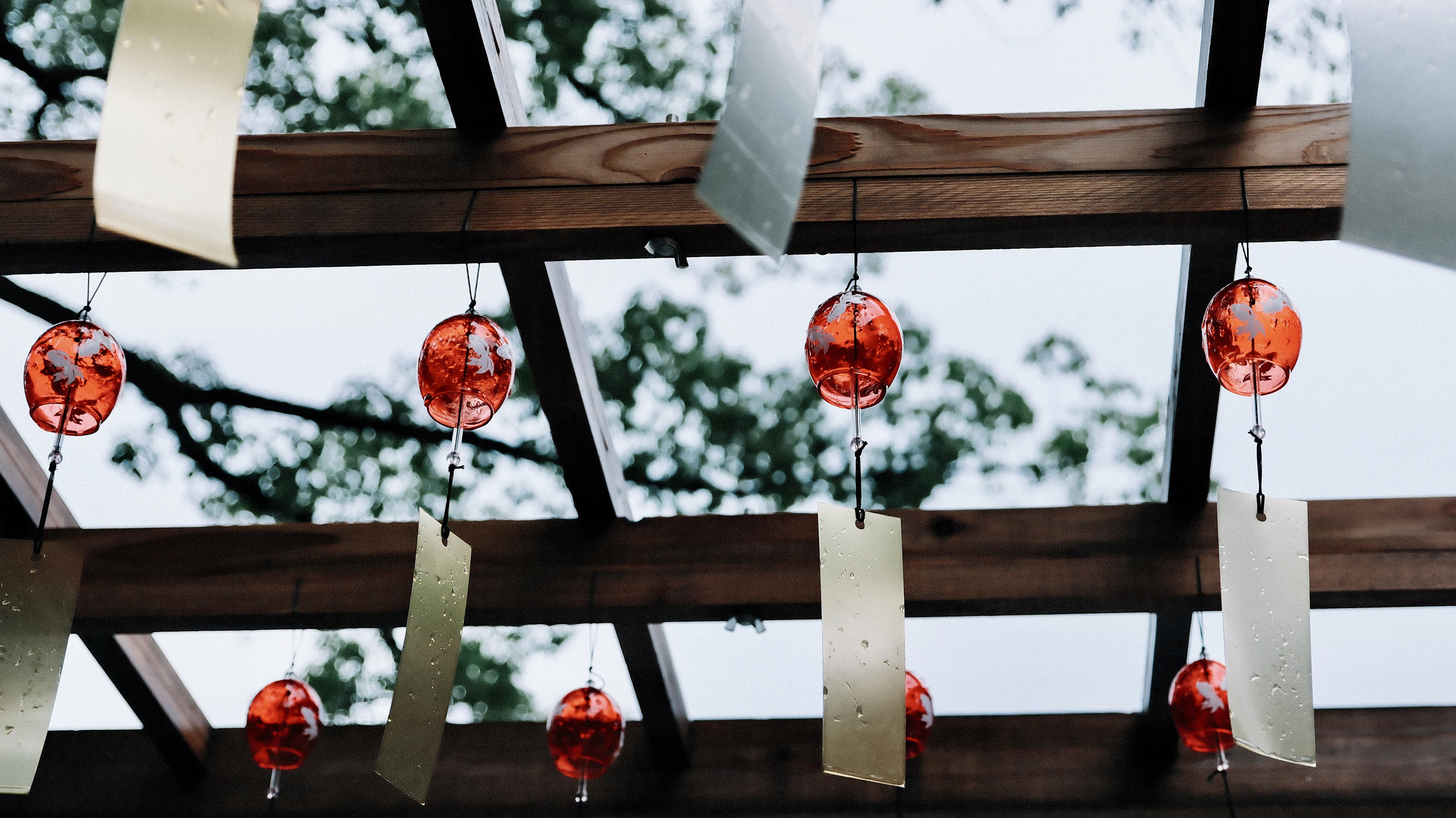 Colorful paper wishes and red ornaments hang from a wooden shrine eave beam.