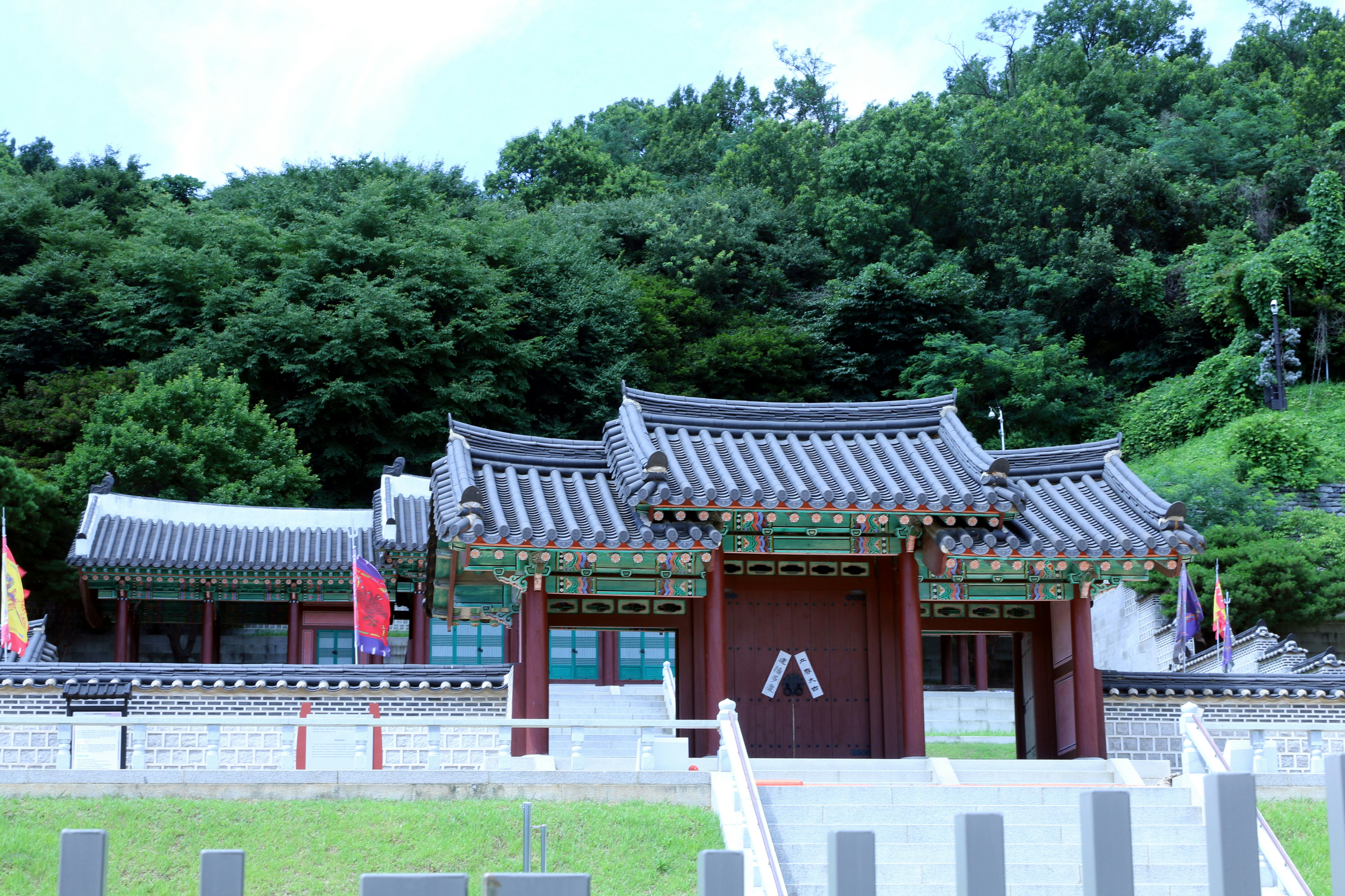 An ornate korean building sits before a green hillside.