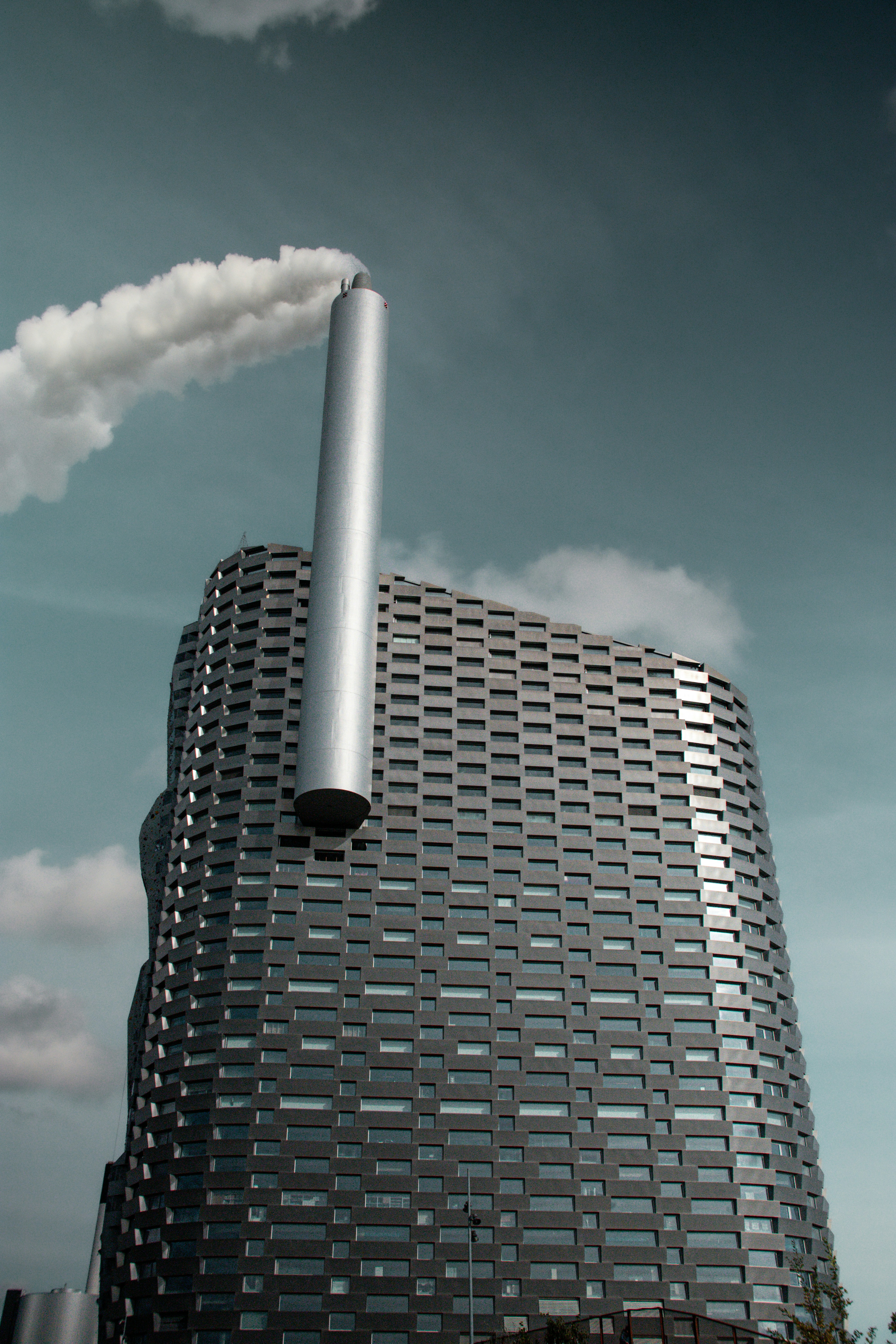 Tall modern building with a smokestack and smoke.