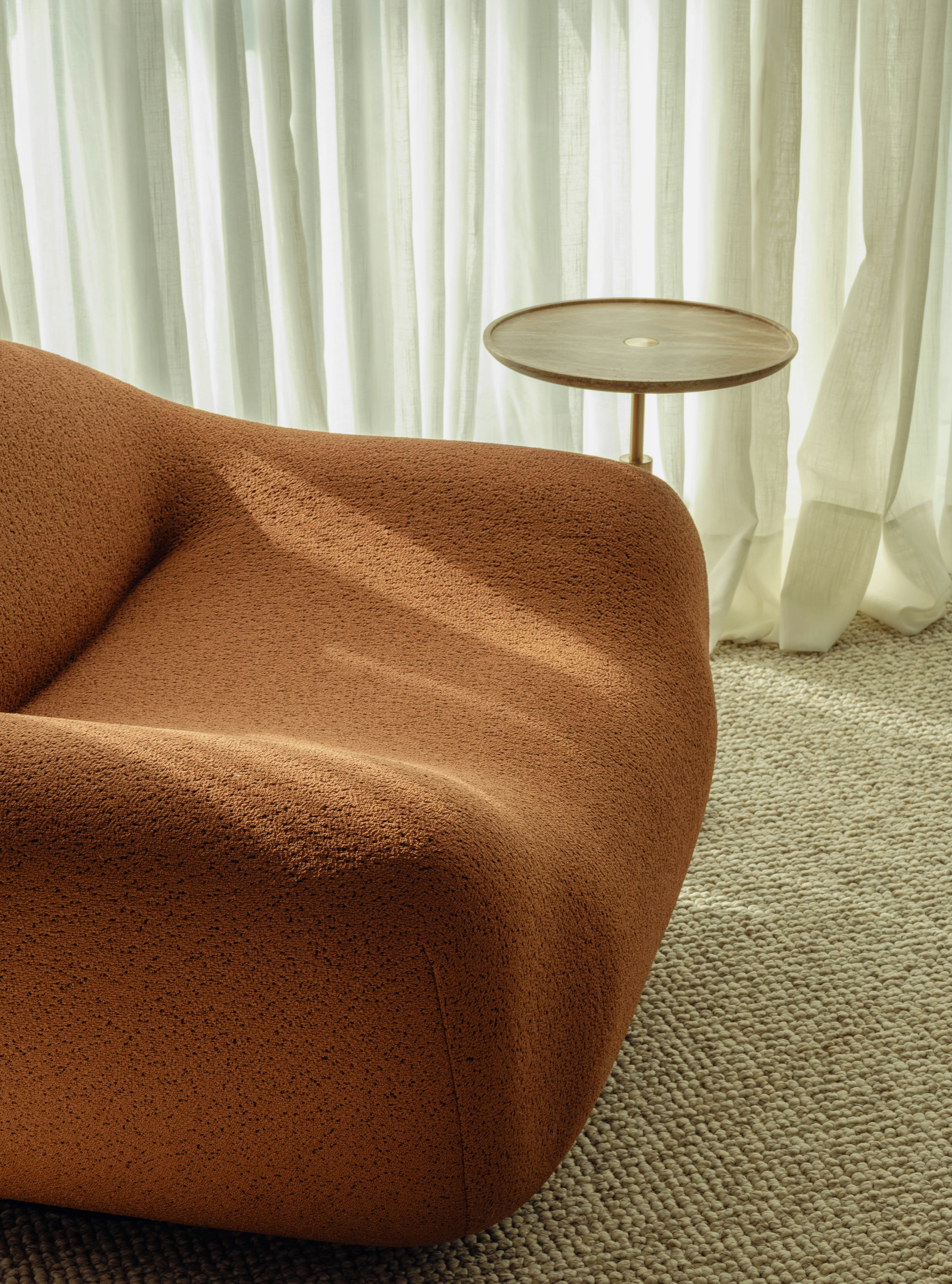 Cozy orange chair near curtains and side table.