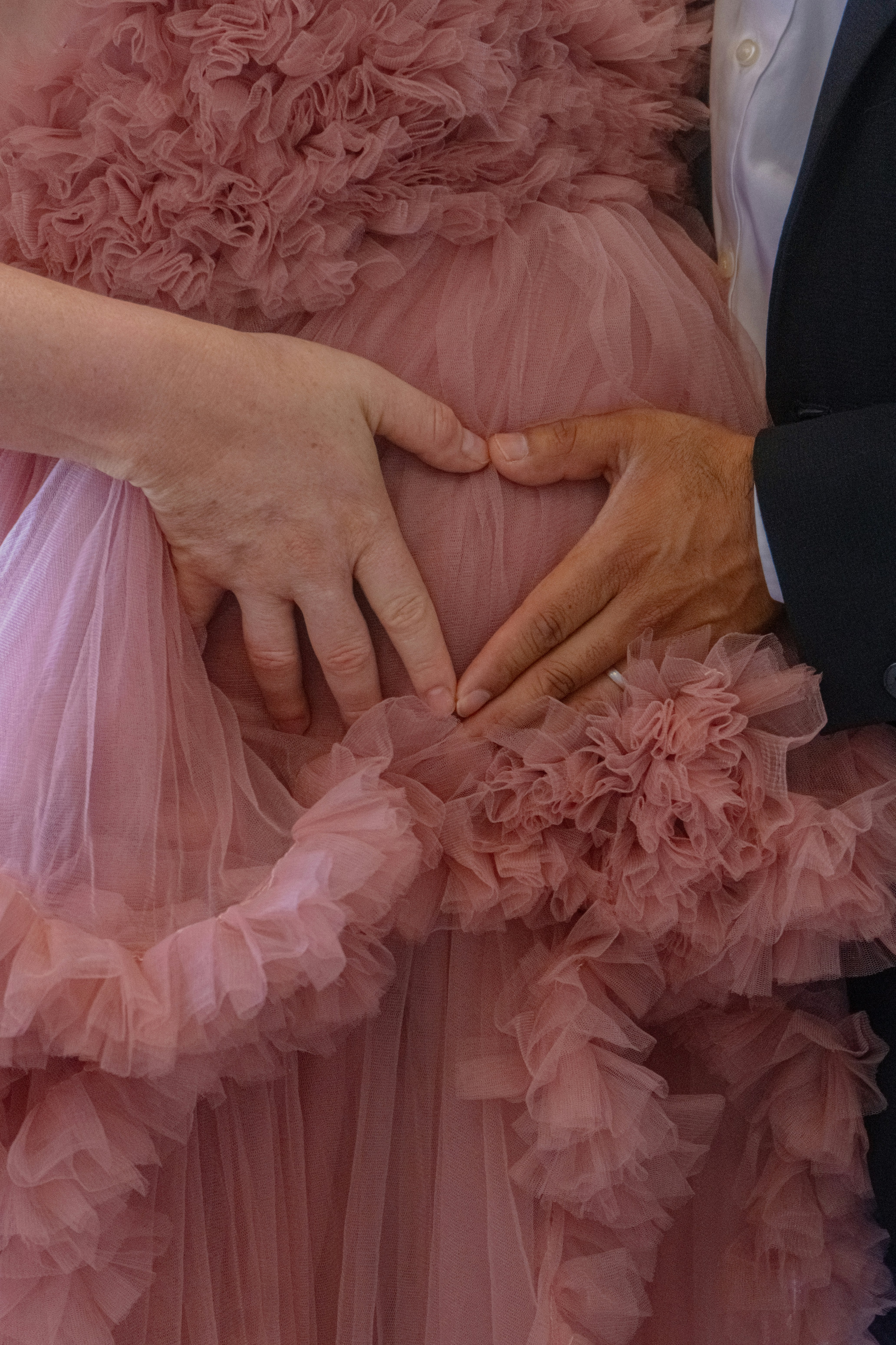 Hands form a heart on a pregnant belly.