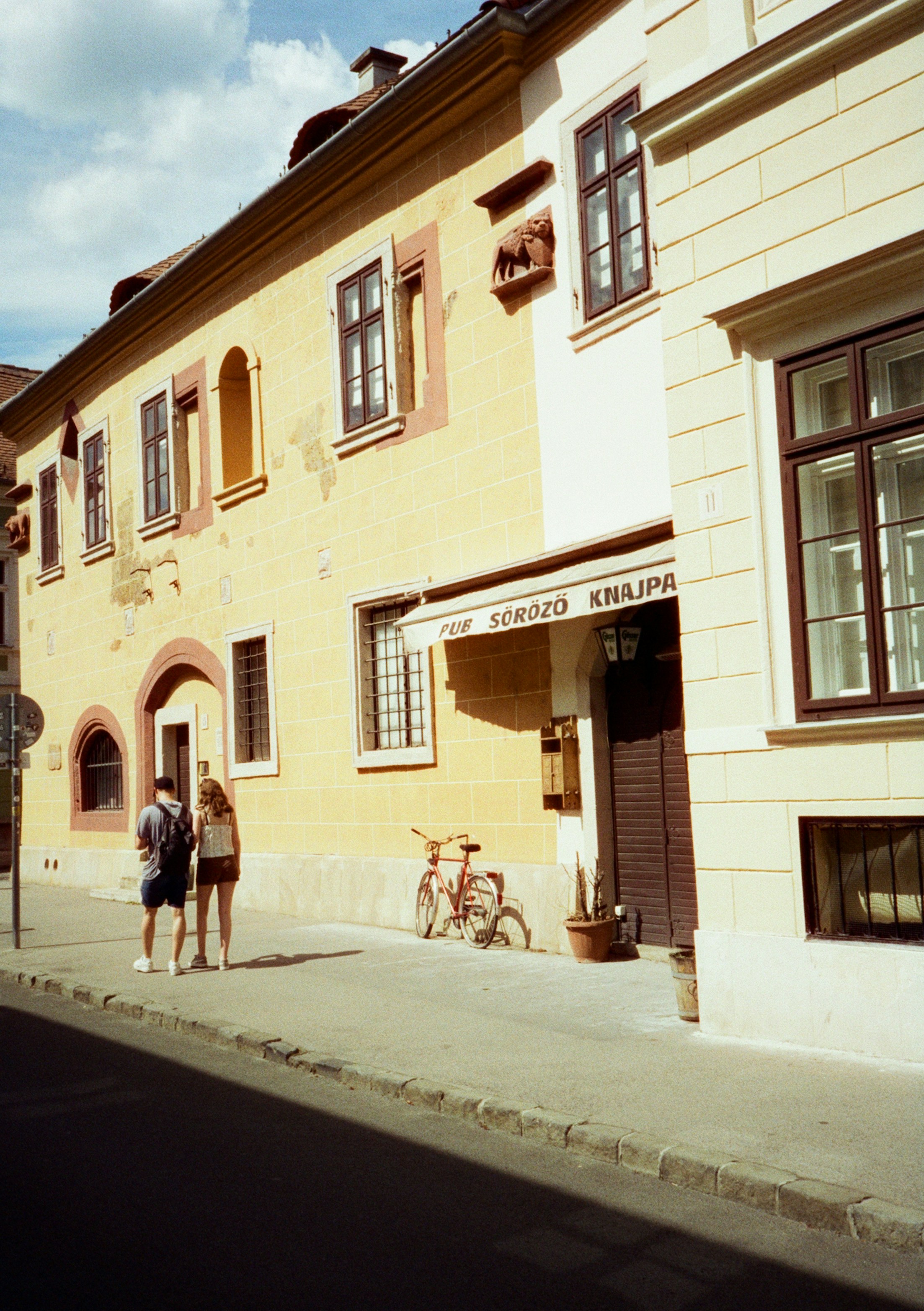People walk past a yellow building on a sunny day