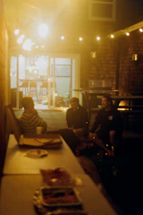 Friends enjoy pizza and drinks in a backyard at night.