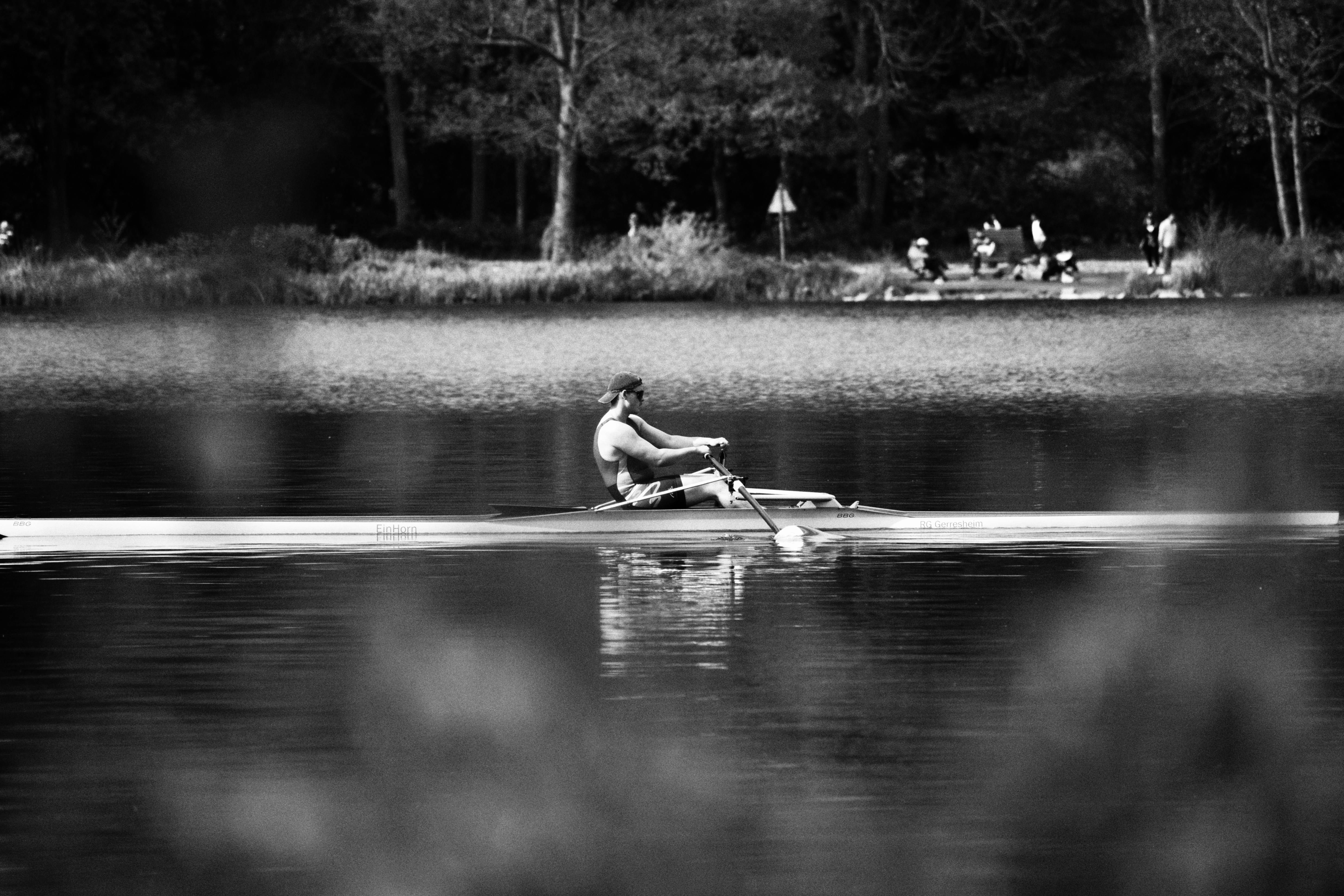 A rower glides across a smooth body of water.