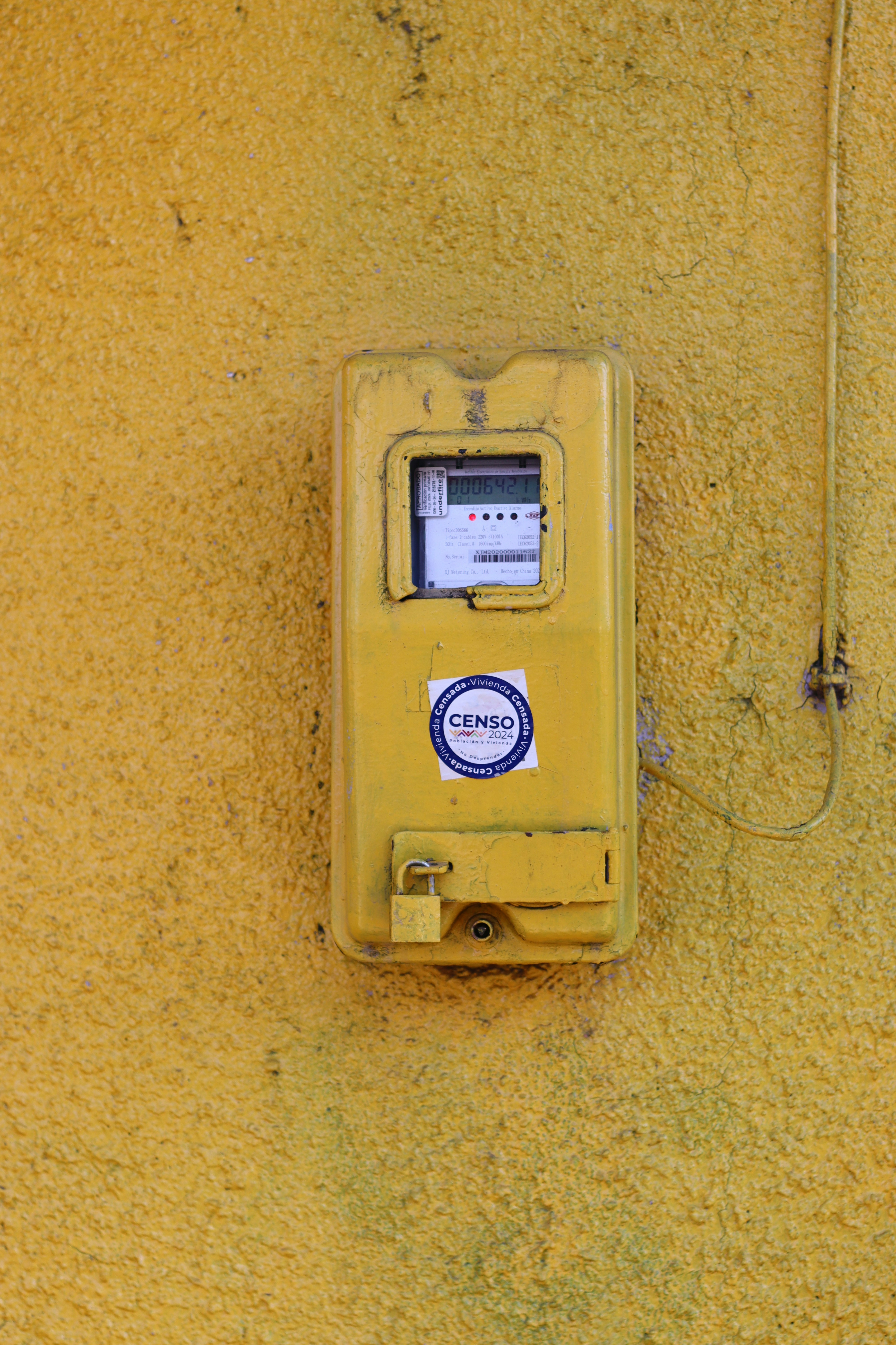 A yellow electric meter is mounted on a yellow wall.