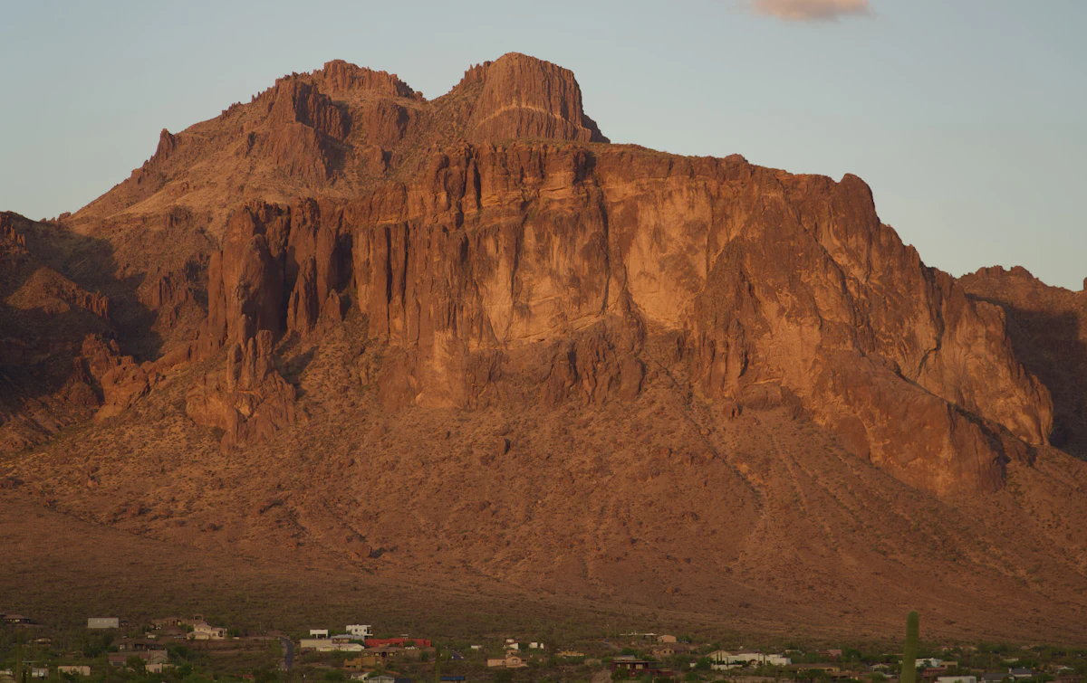 The cliffs of the Superstition Mountains lit gold, with houses along their foot